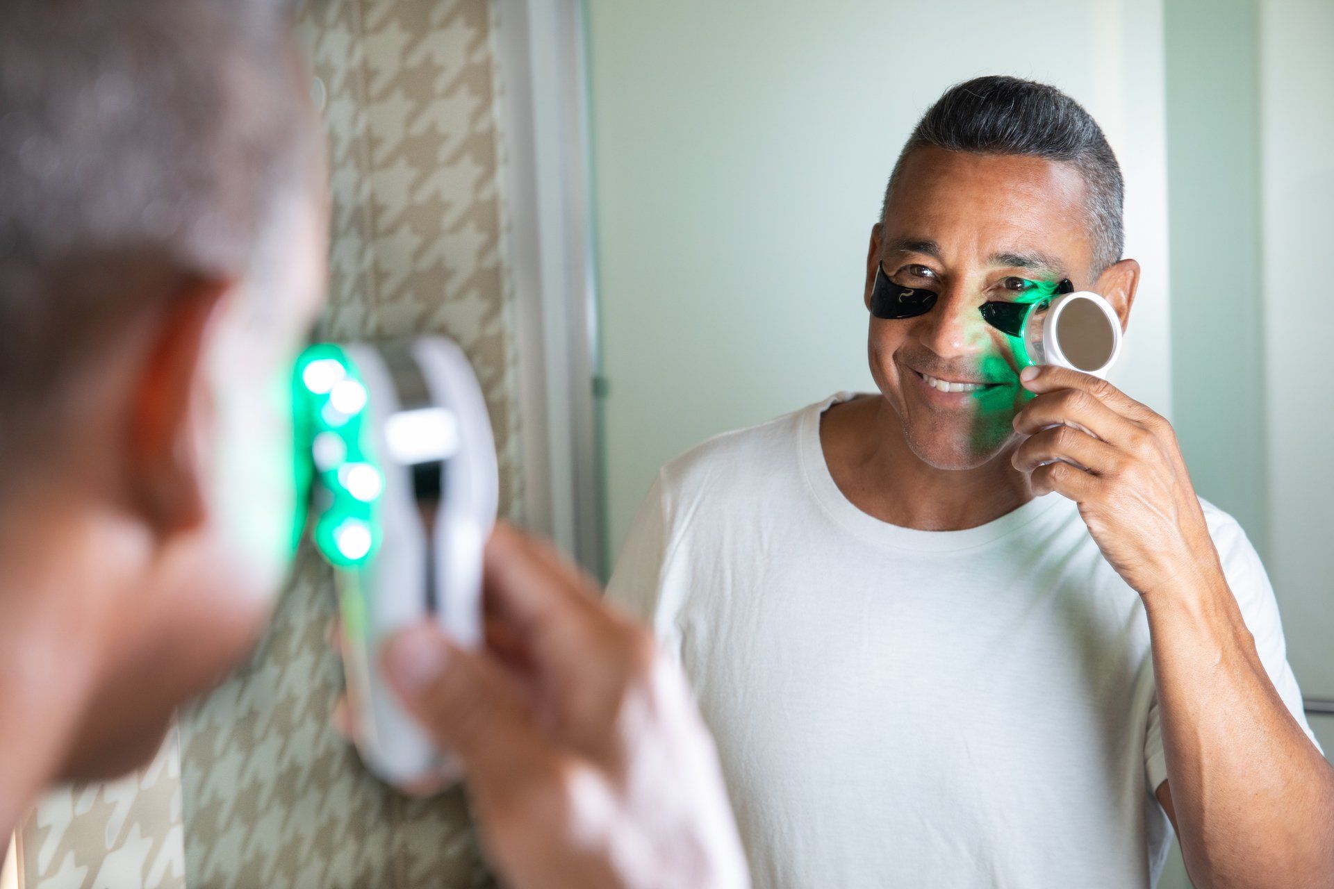 A man is applying a black mask to his face in front of a mirror