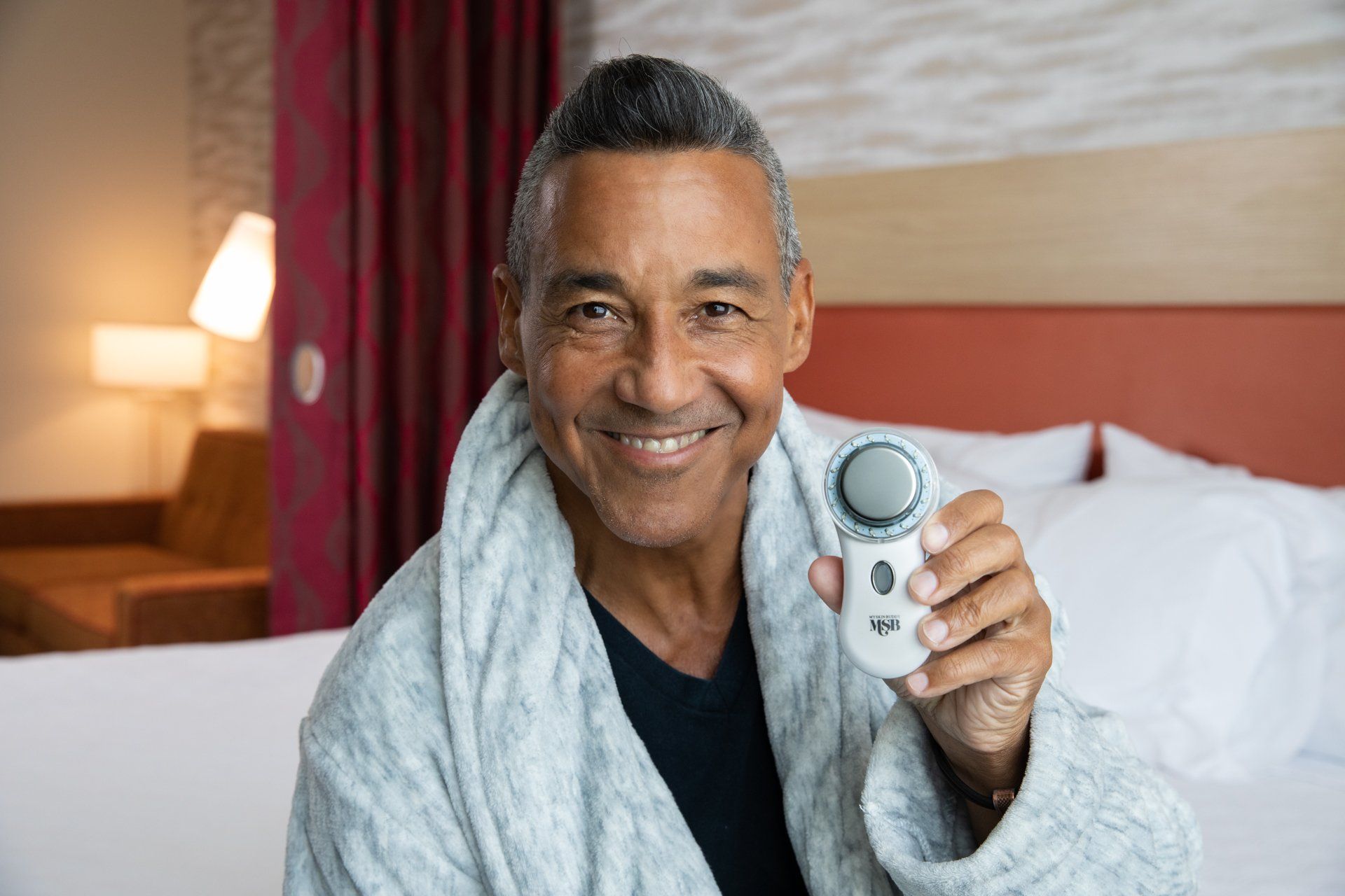 A man in a bathrobe is sitting on a bed holding a device