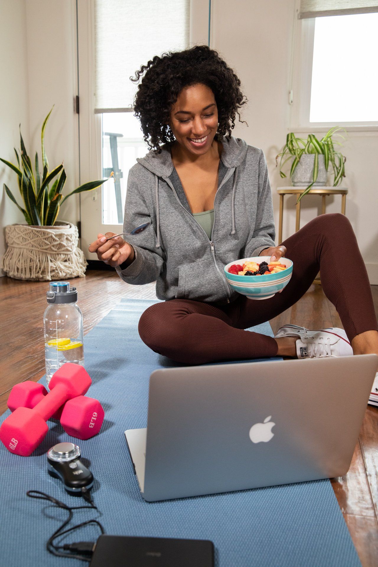 A woman is sitting on a yoga mat in front of an apple laptop
