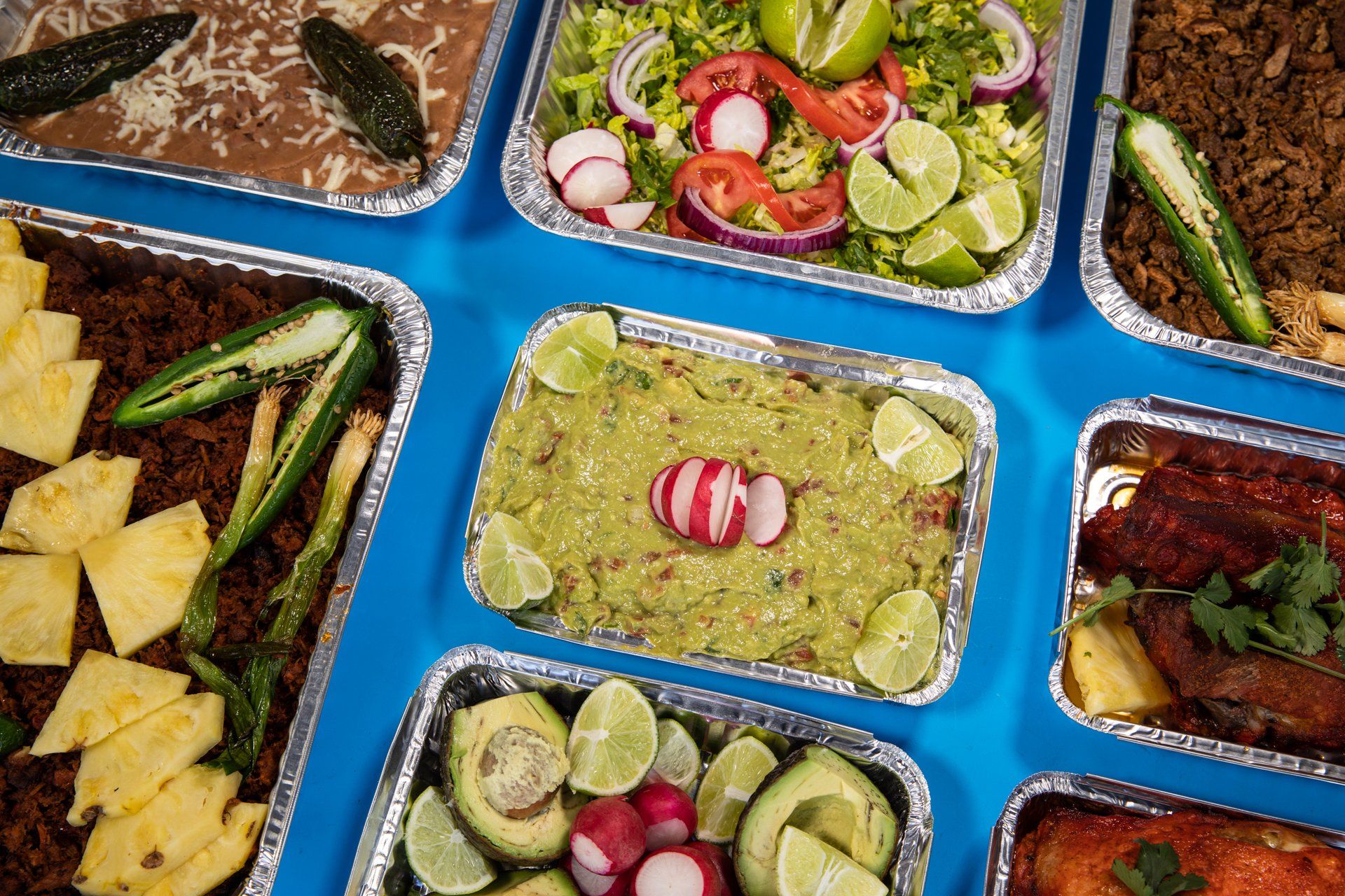 A variety of food in aluminum foil containers on a blue table