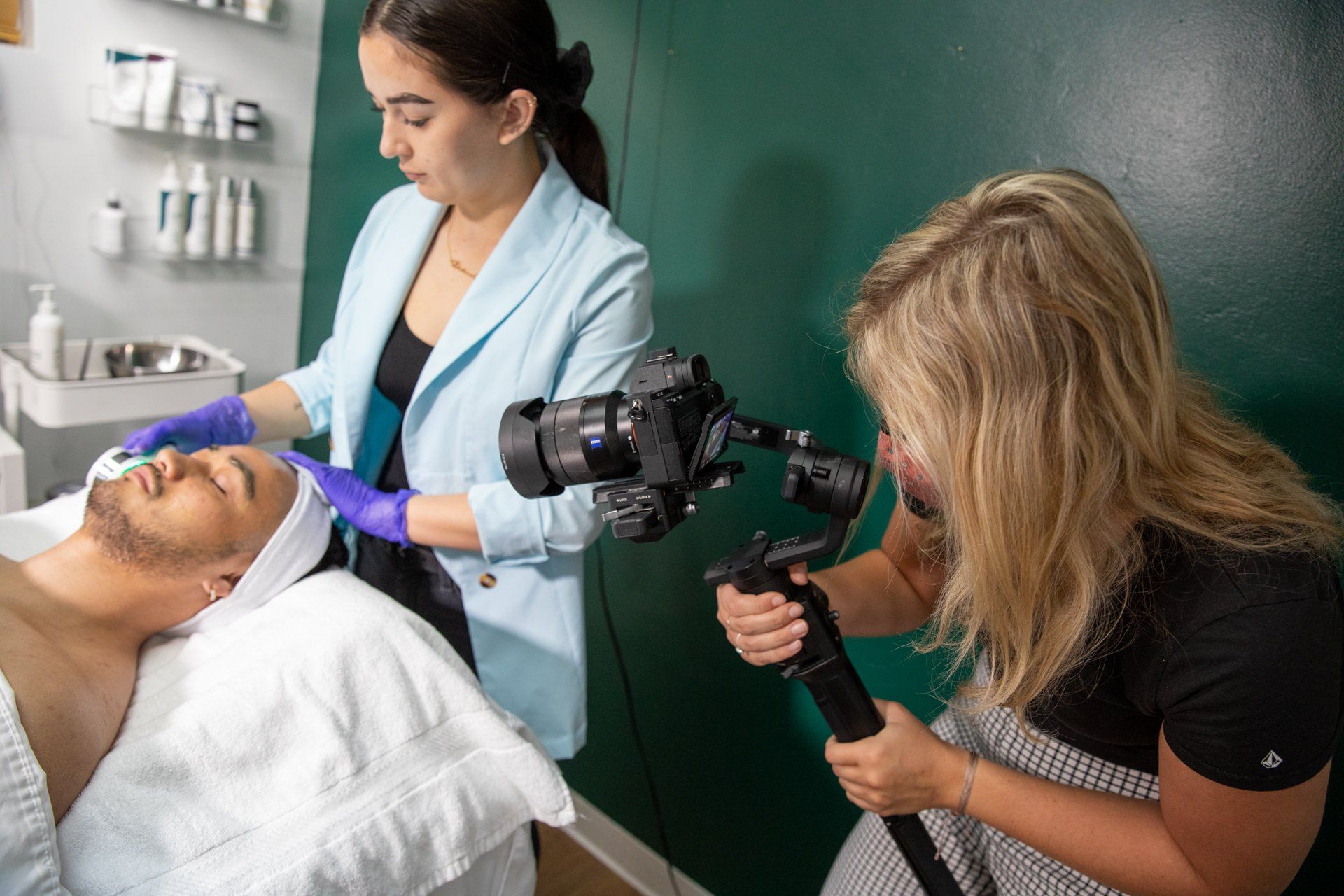 A woman is taking a picture of a man getting a facial treatment