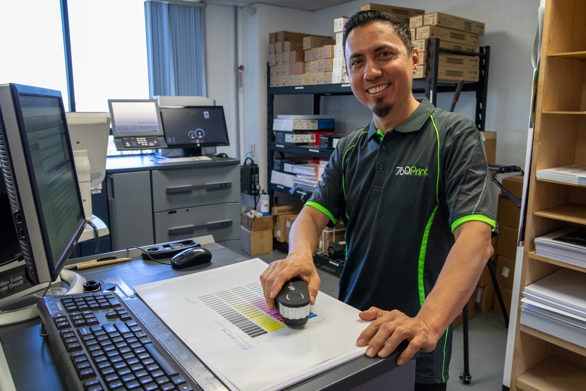 A man in a black and green shirt is standing in front of a computer