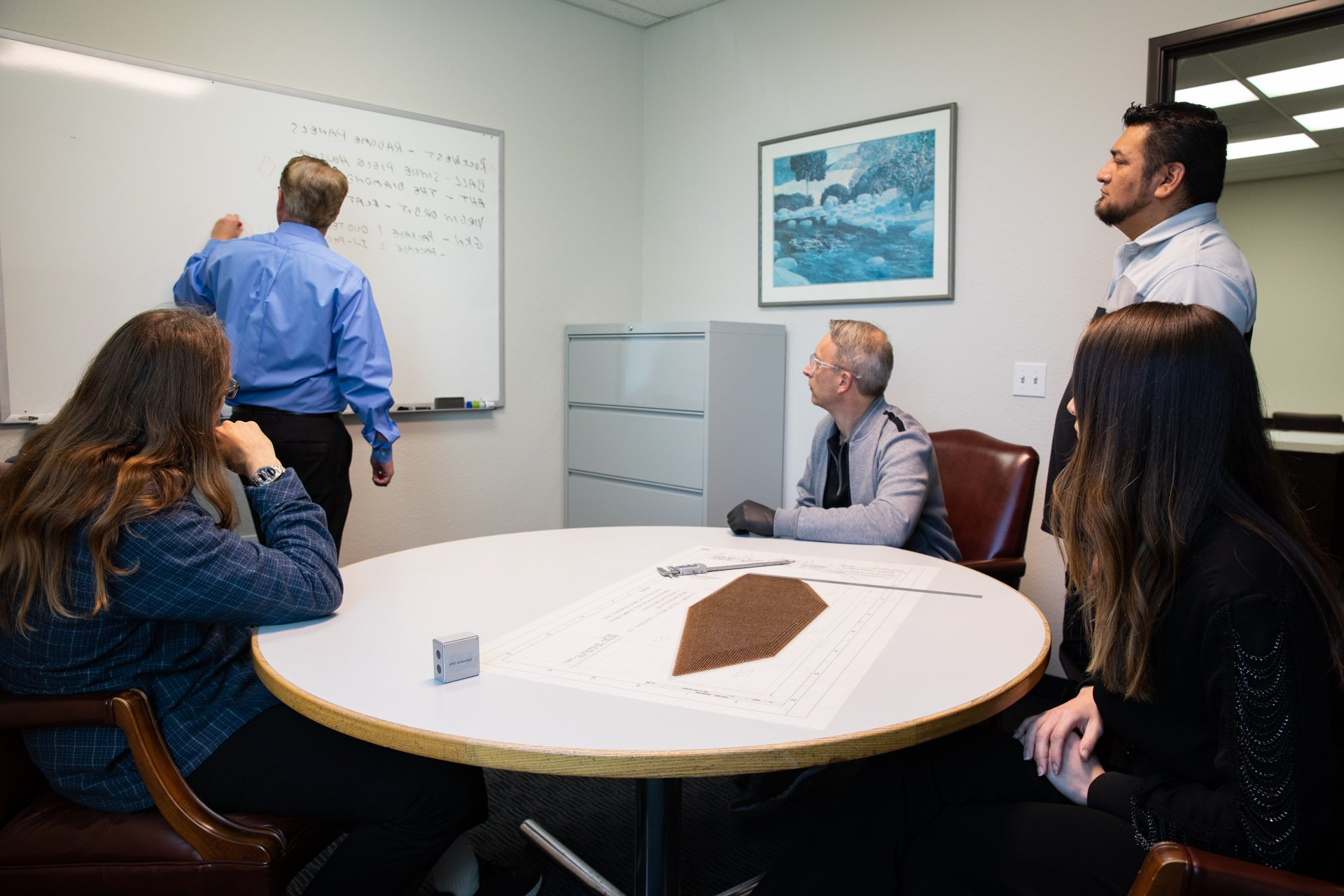 A group of people sitting around a table in front of a whiteboard