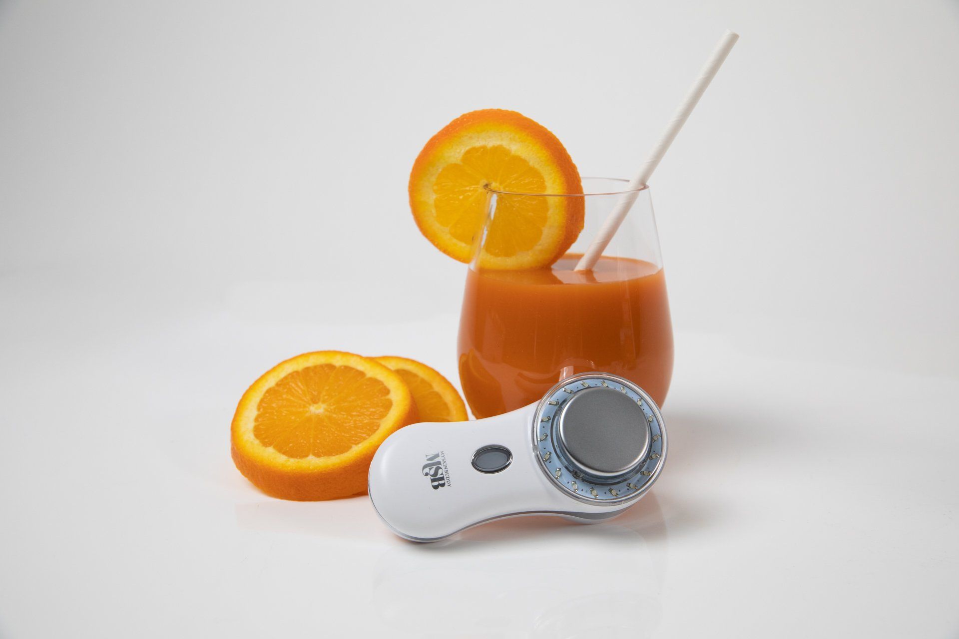 A glass of orange juice next to oranges and a device
