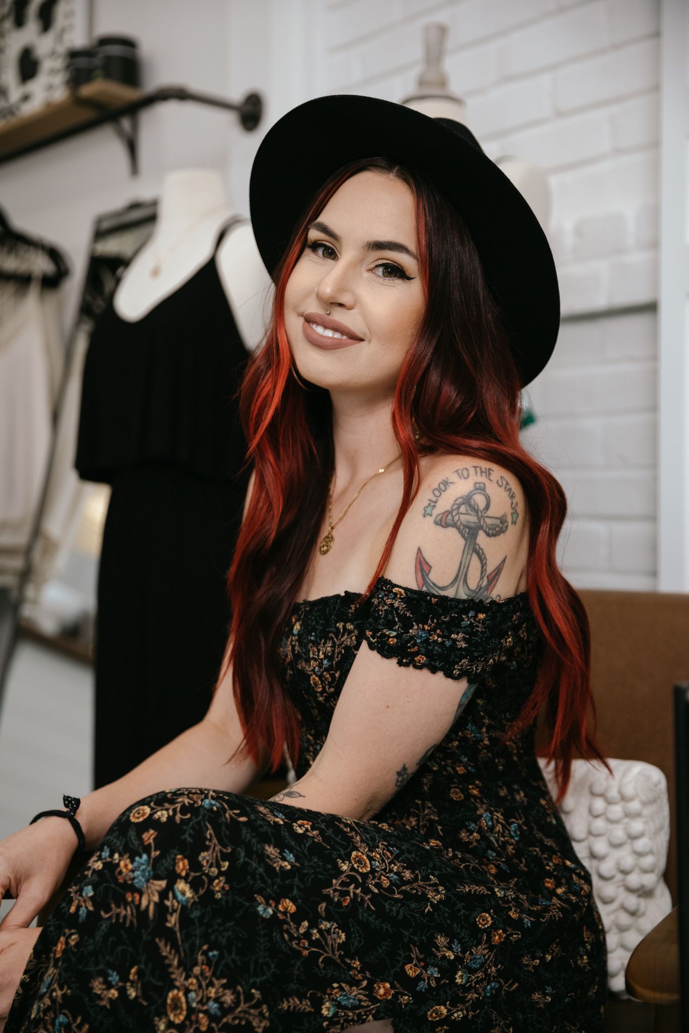 A woman with red hair is wearing a black hat and a black dress
