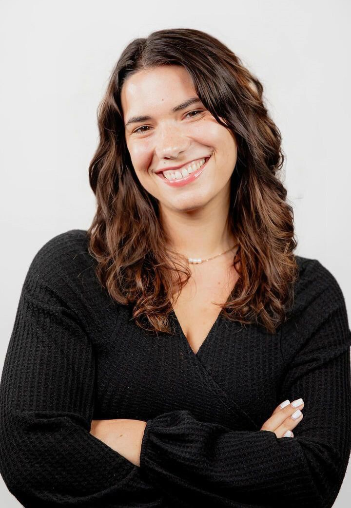 A woman in a black sweater is smiling with her arms crossed.