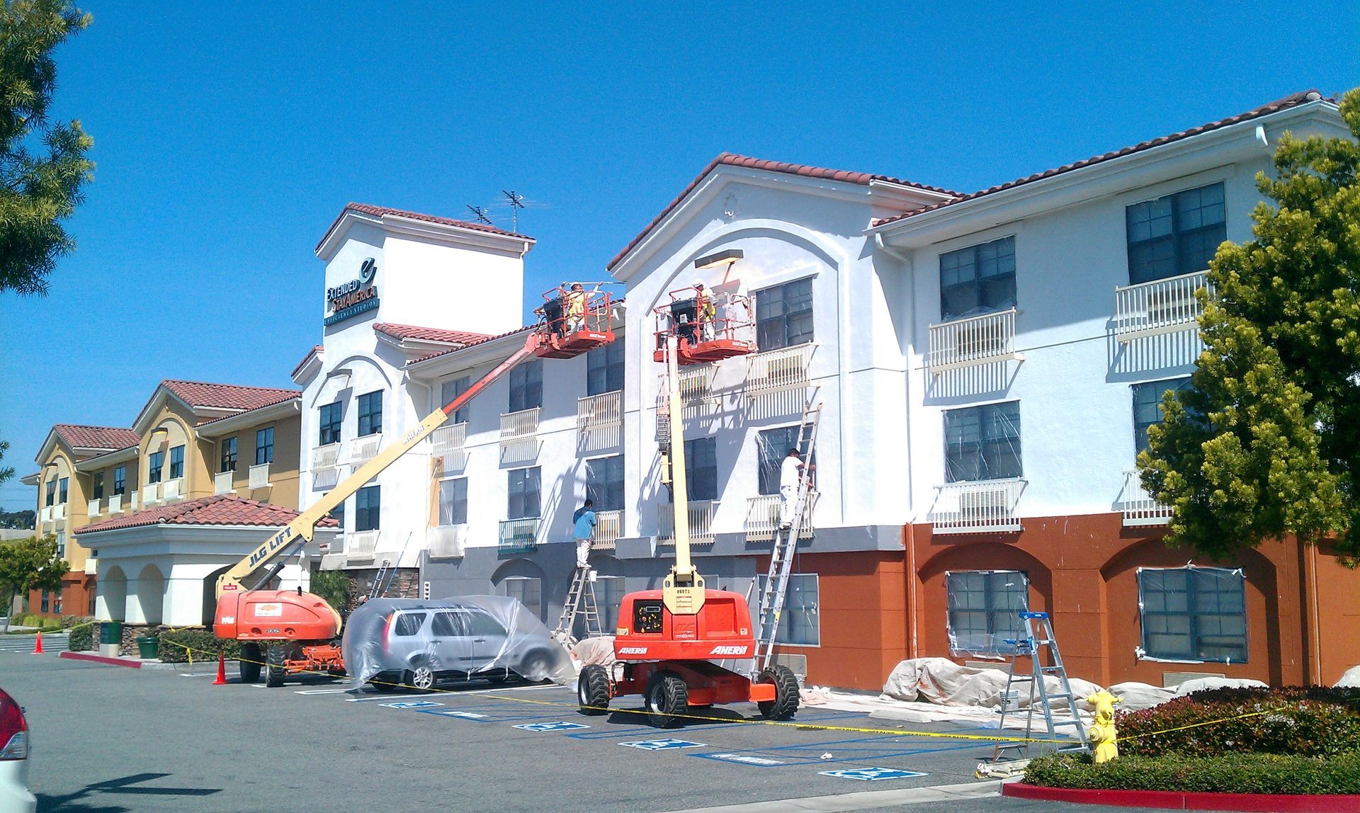 A large building is being painted with a crane
