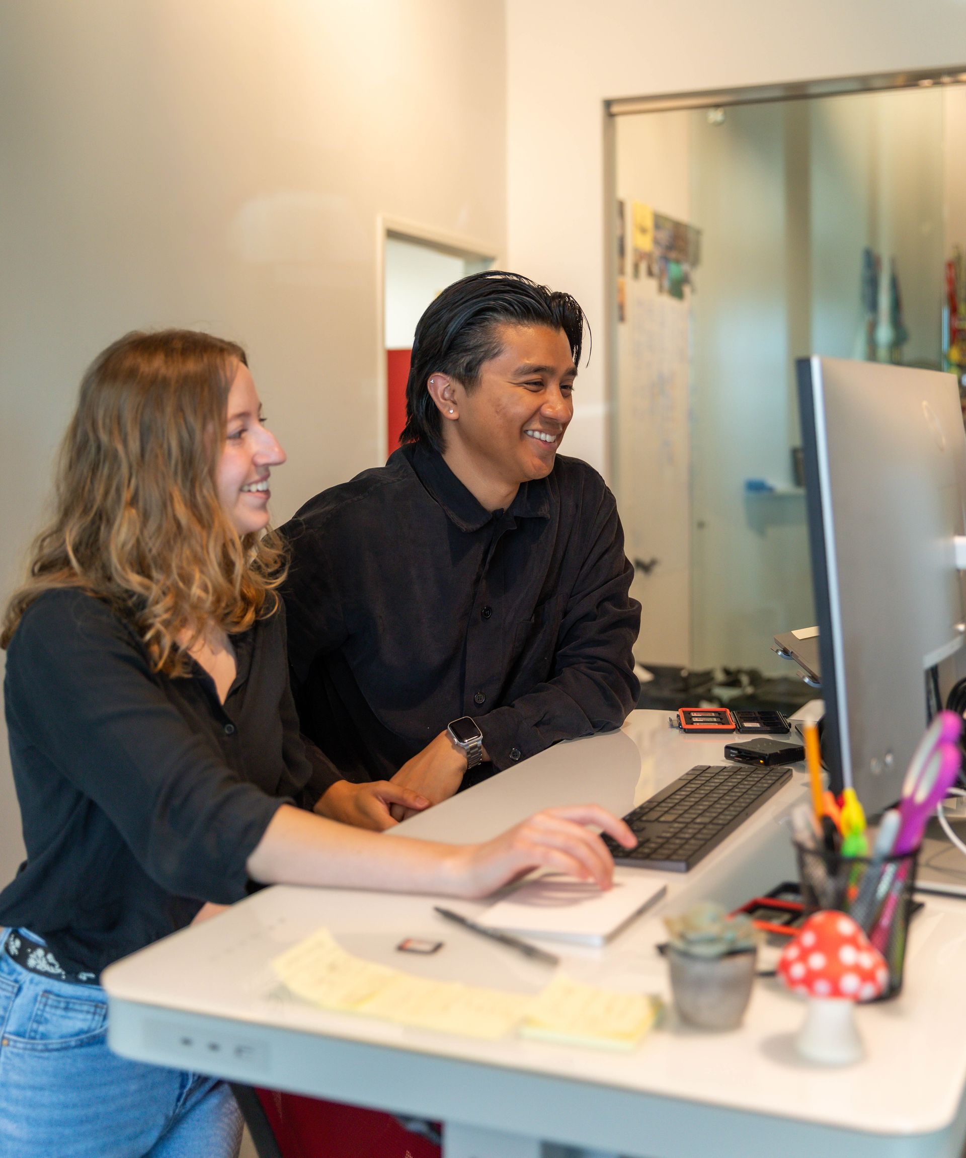 A man wearing glasses is smiling while sitting at a desk