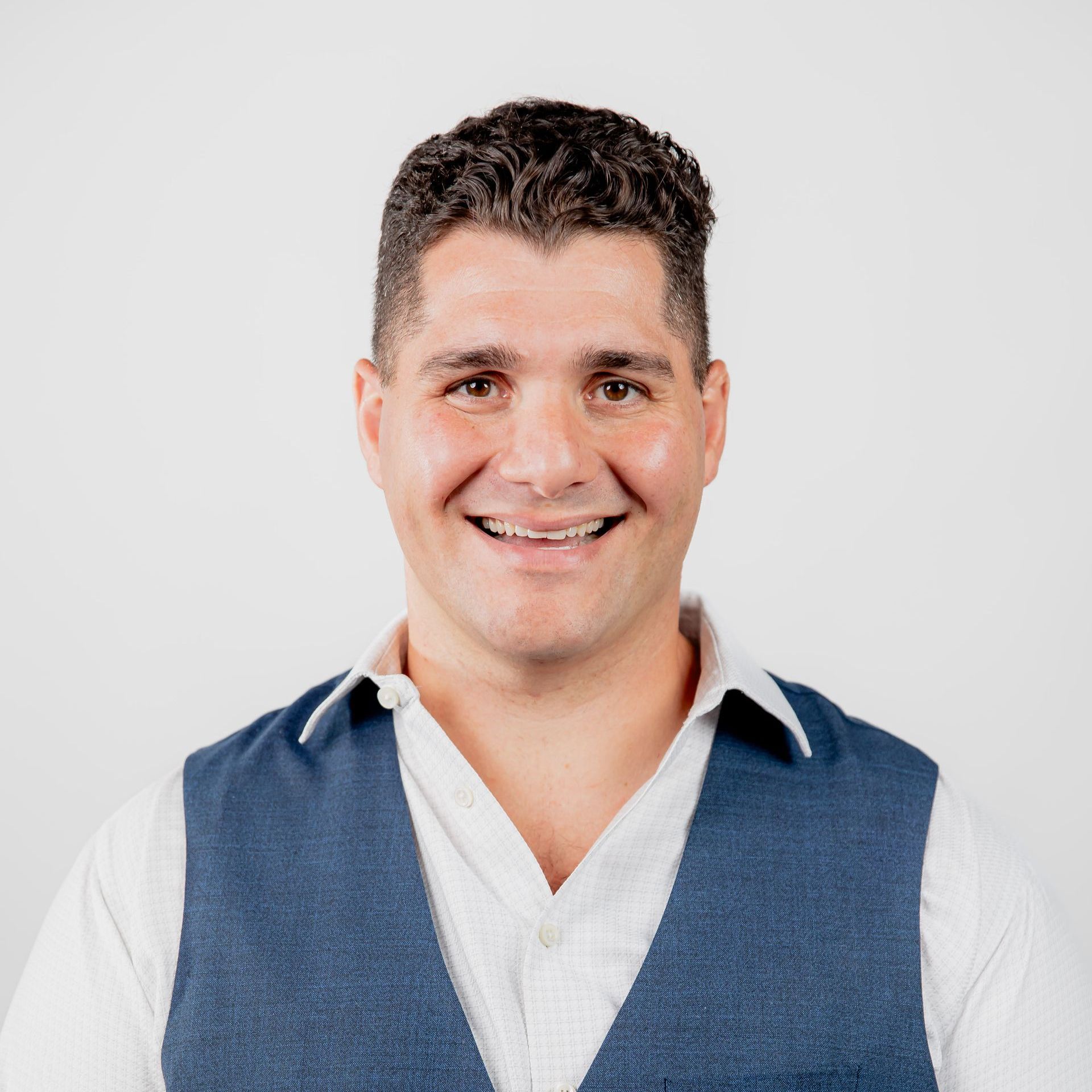 A man wearing a white shirt and a blue vest smiles for the camera