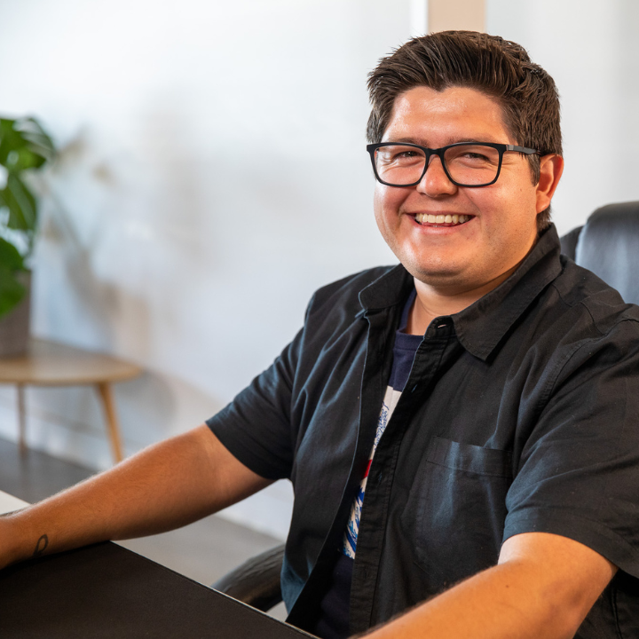 A man wearing glasses is smiling while sitting at a desk