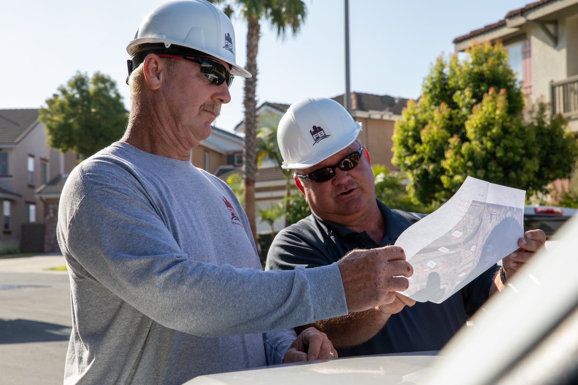 Two men wearing hard hats are looking at a piece of paper