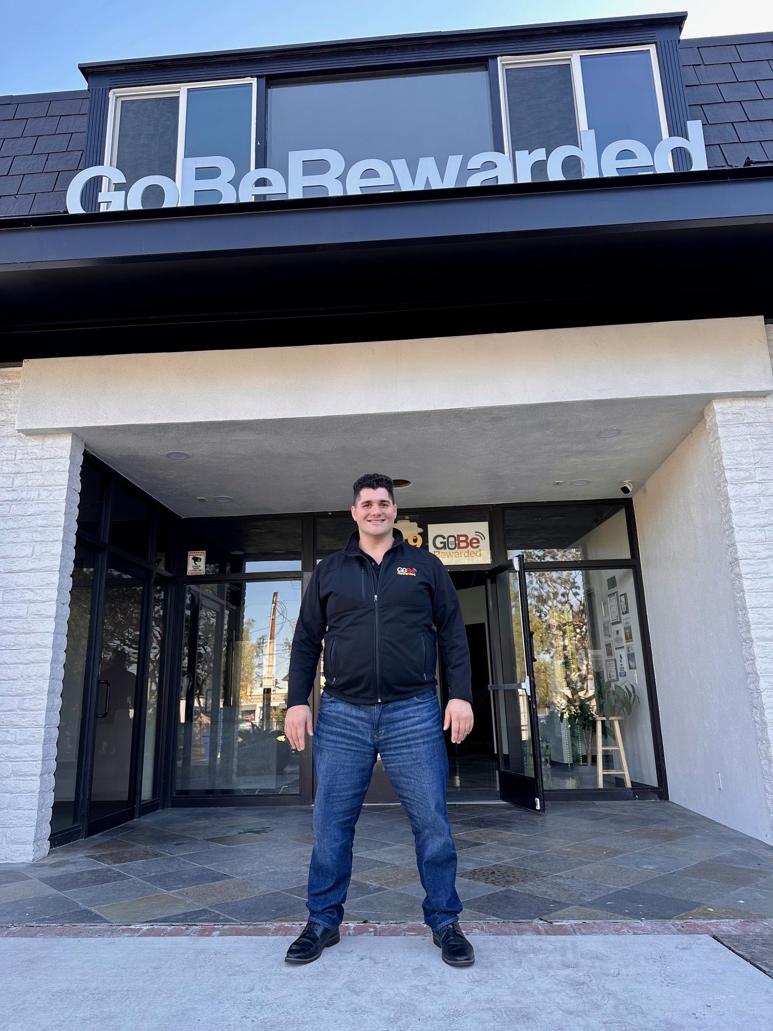 A man standing in front of a building that says go be rewarded