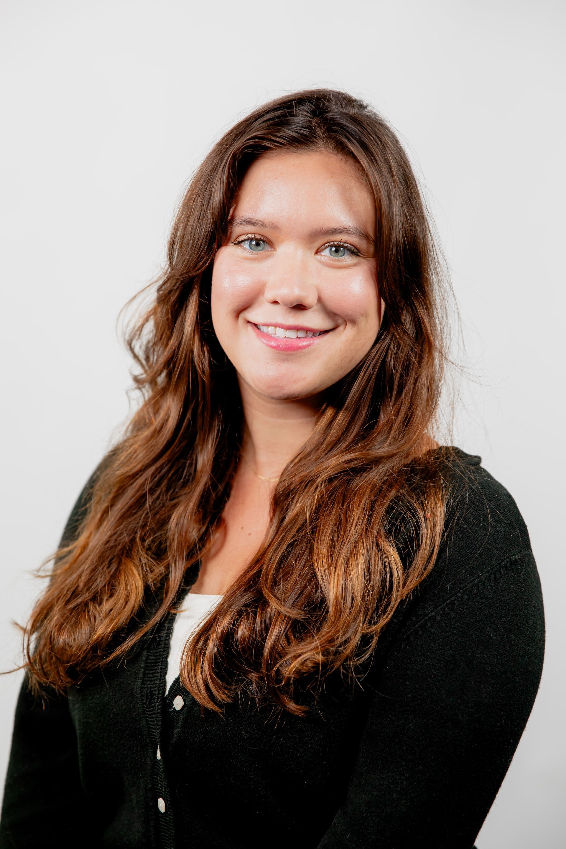 A woman with long brown hair is smiling and wearing a black sweater