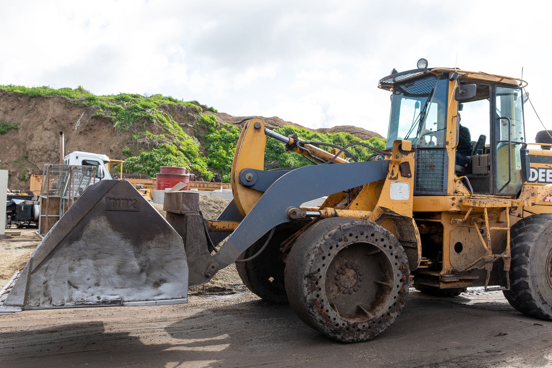 A yellow tractor with a large bucket is parked in a dirt lot