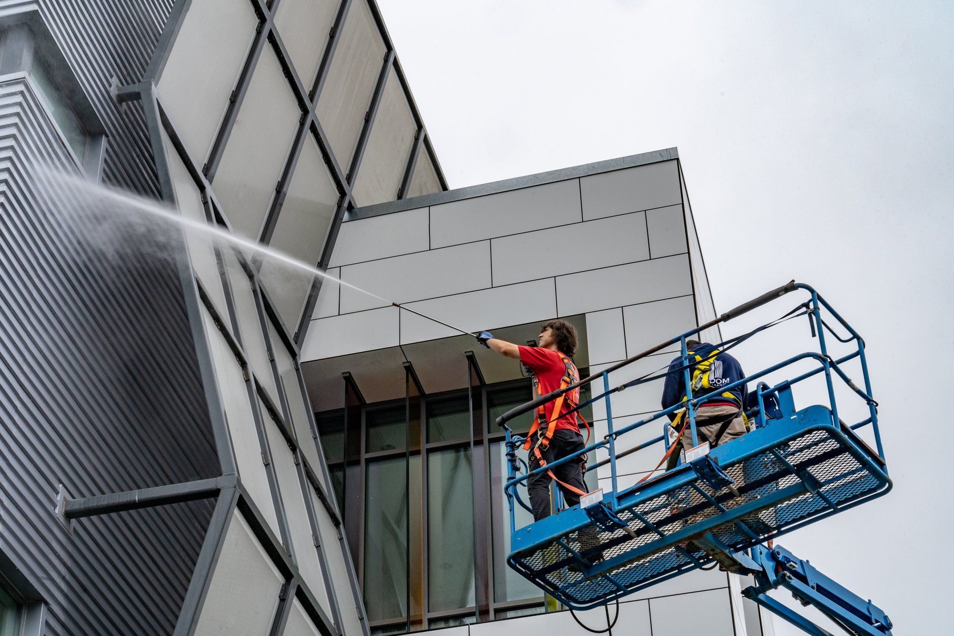 Two men are cleaning a building with a high pressure washer