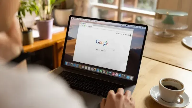 A person is typing on a laptop computer while sitting at a table with a cup of coffee.