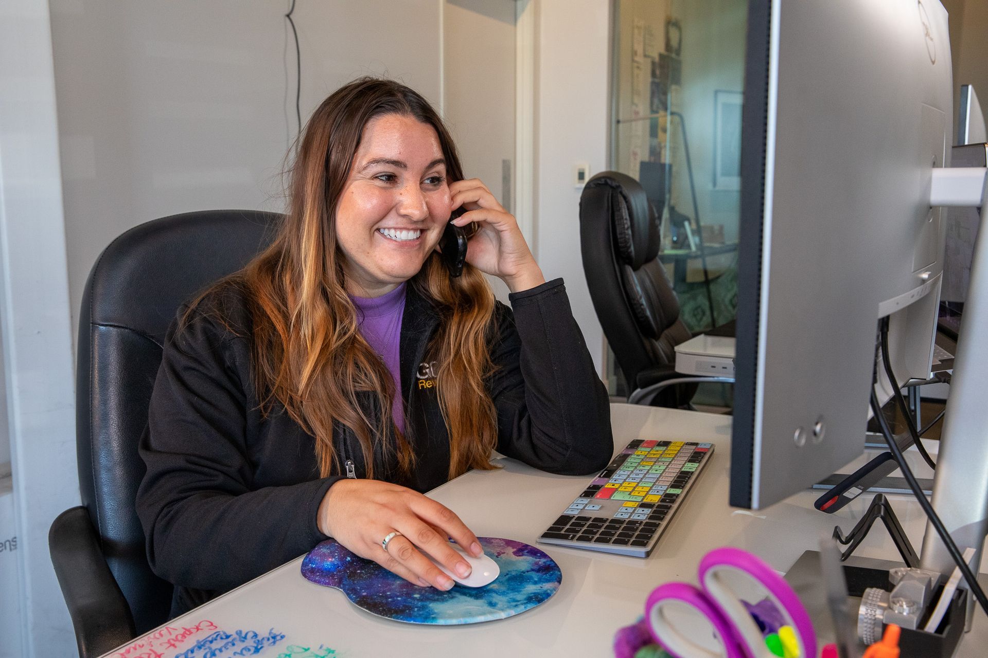 A woman is sitting at a desk talking on a cell phone.