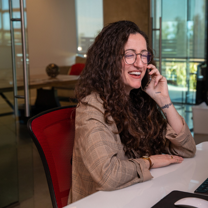 A woman wearing glasses is smiling while talking on a cell phone