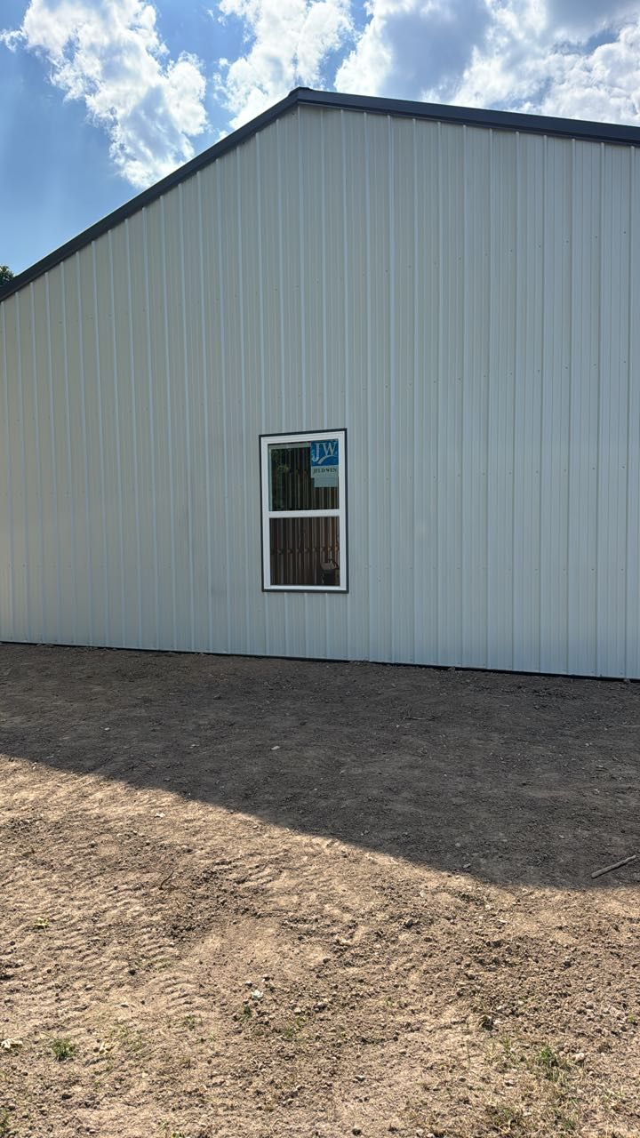 White metal-sided building exterior with a single rectangular window centered on the wall above a dirt ground.