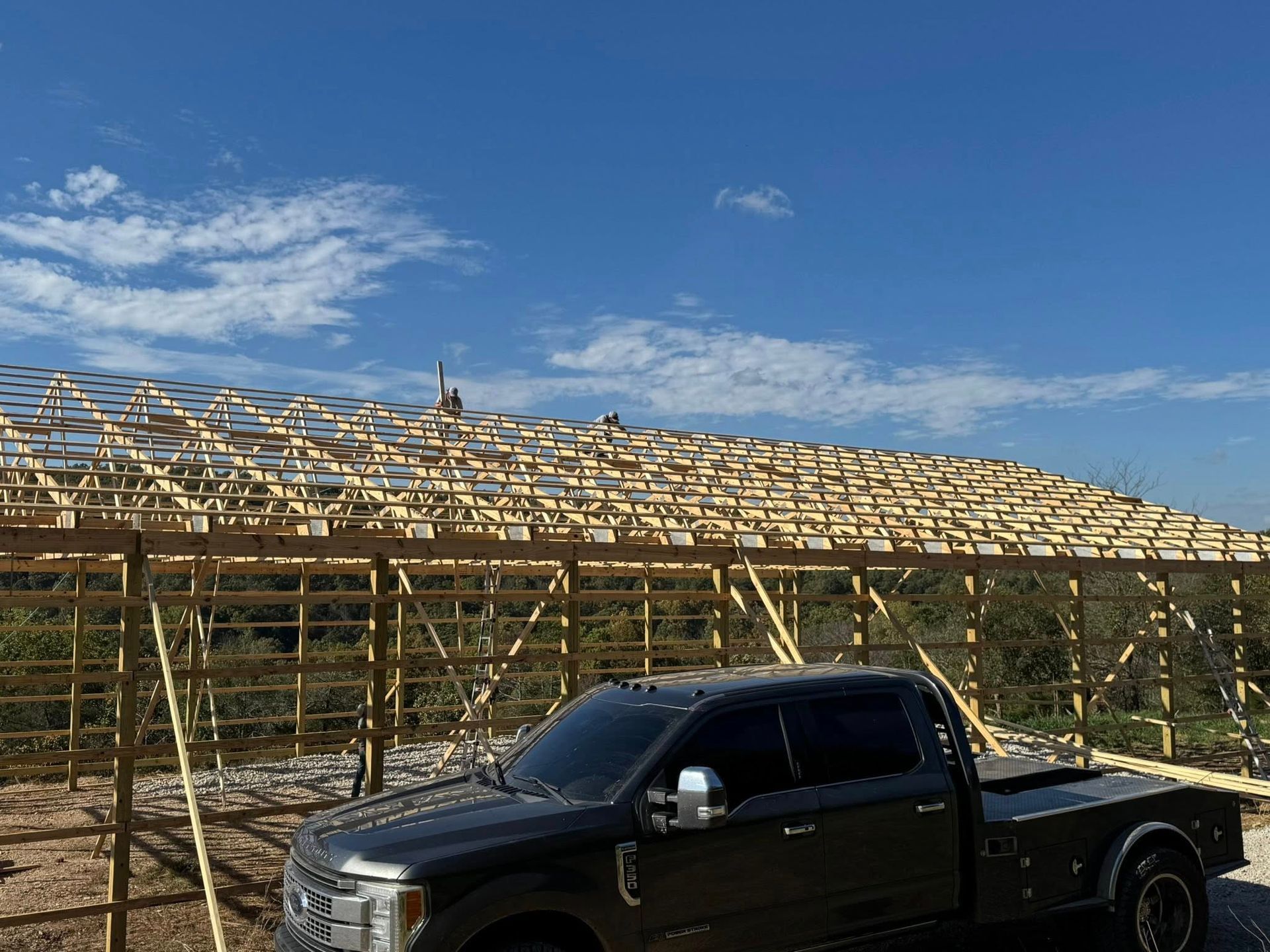 A dark-colored pickup truck is parked in front of a partially constructed wooden building frame under a clear blue sky.