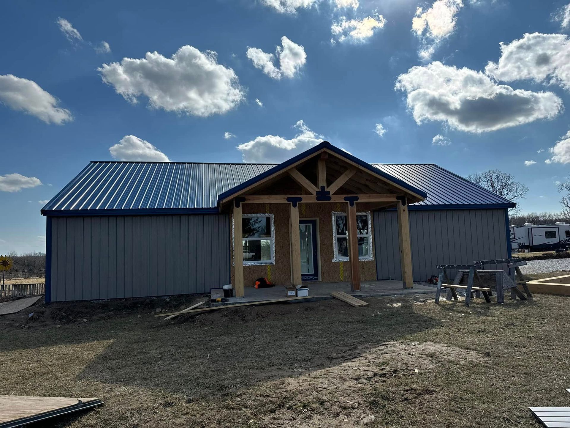 A newly constructed gray metal-sided house with a dark blue corrugated metal roof and a covered wooden front porch.