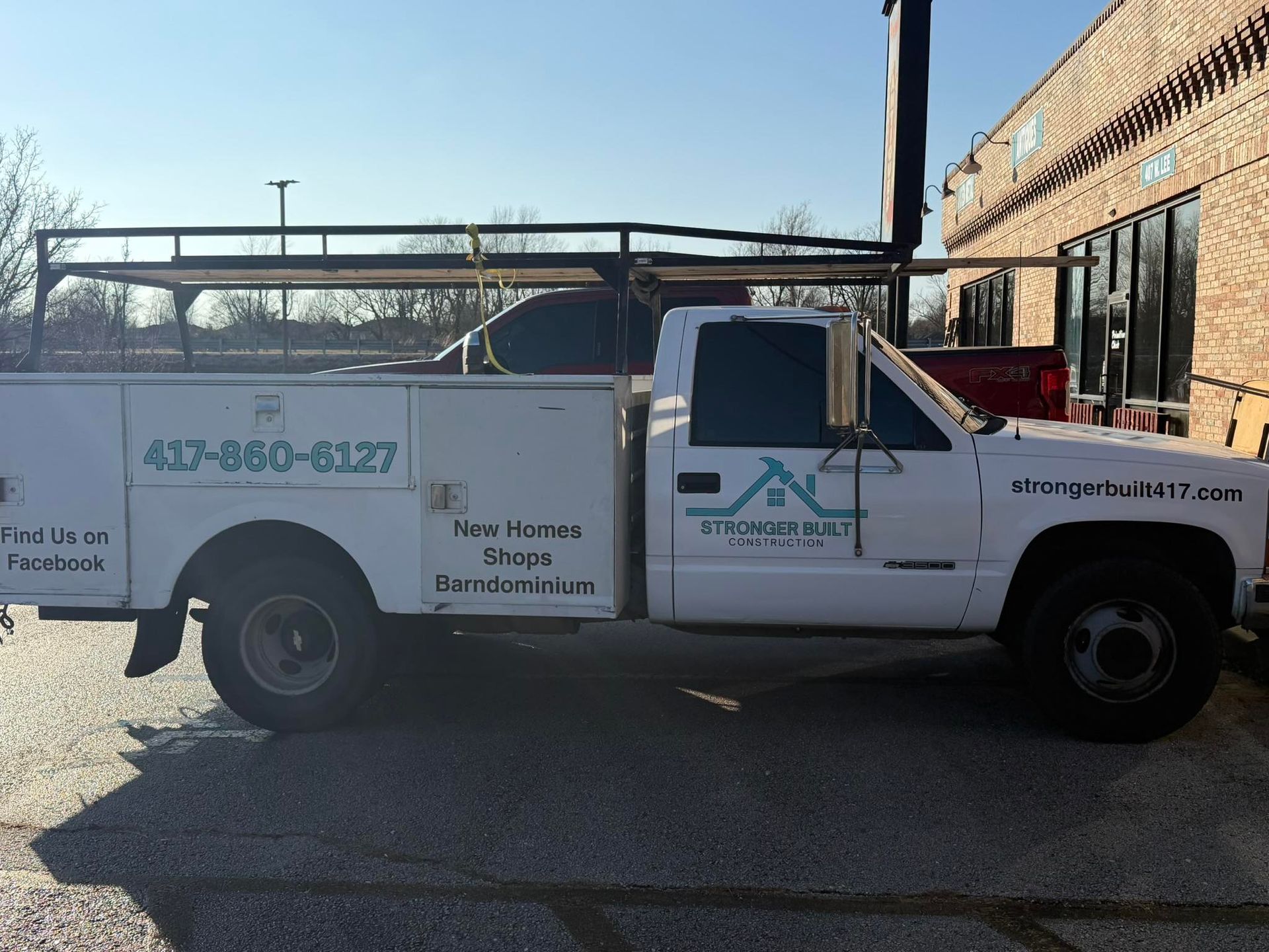 A white utility truck parked in a lot, featuring business branding, a phone number, and a roof rack.
