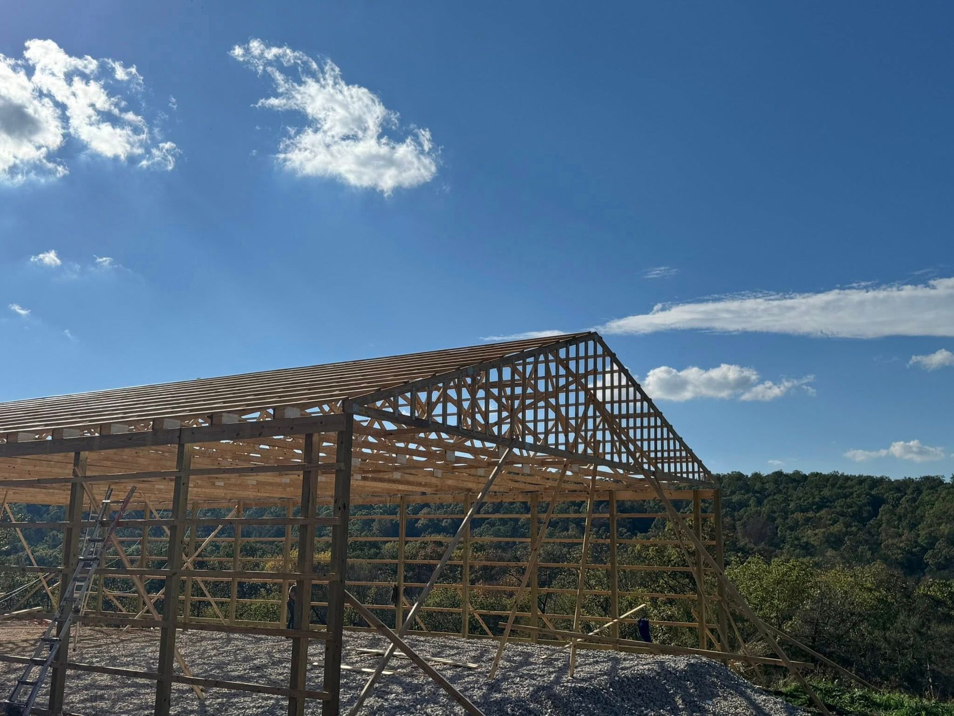 A wooden frame of a building under construction against a bright blue sky with scattered clouds.