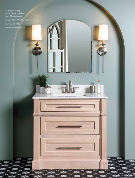 Bathroom vanity with light wood cabinet, marble countertop, and arched mirror, flanked by sconces on a teal-colored wall.