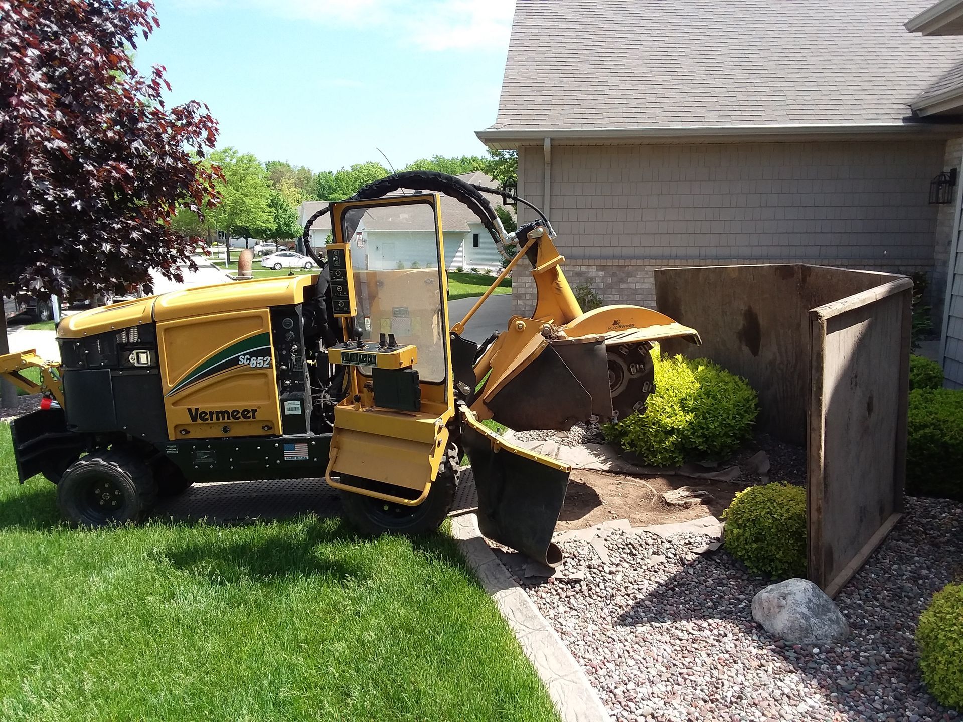 A yellow stump grinder cuts into a tree stump, creating wood chips on the ground outdoors.