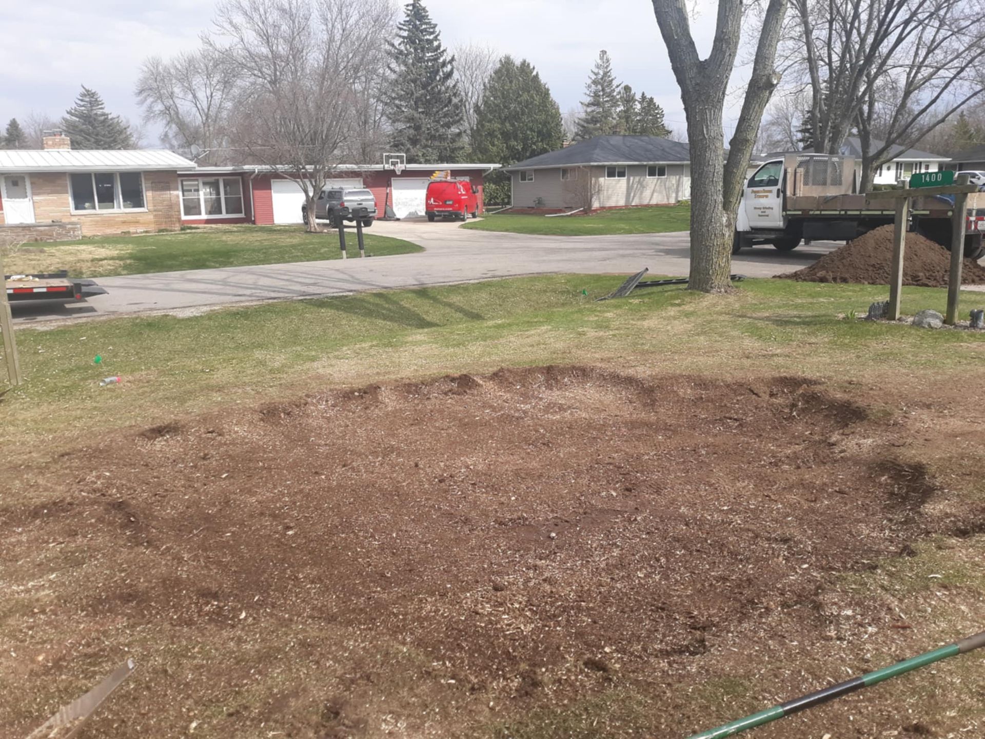 A yellow stump grinder cuts into a tree stump, throwing wood chips in an outdoor residential setting.