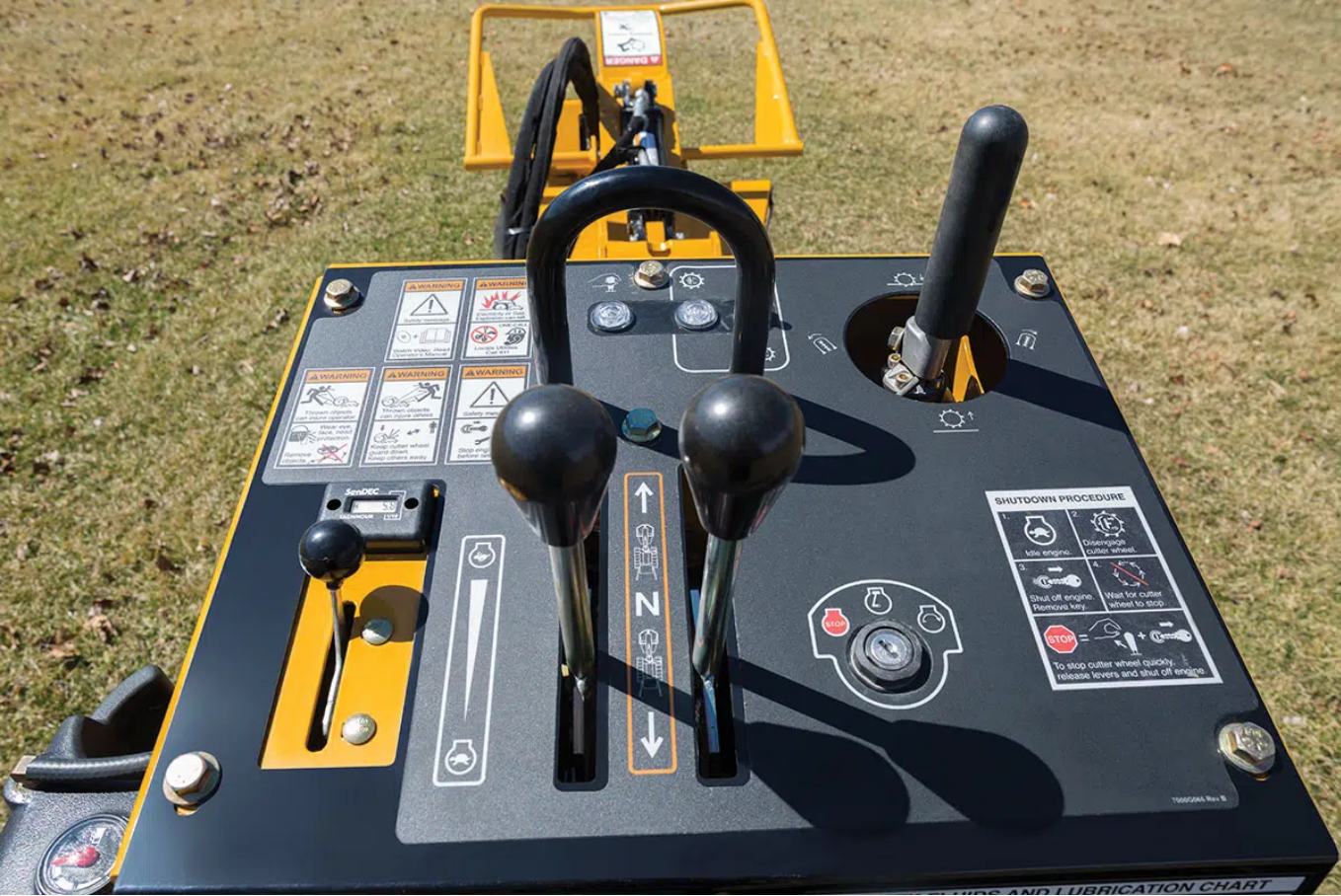 The control panel of a yellow construction machine featuring various levers, buttons, and safety instruction decals.