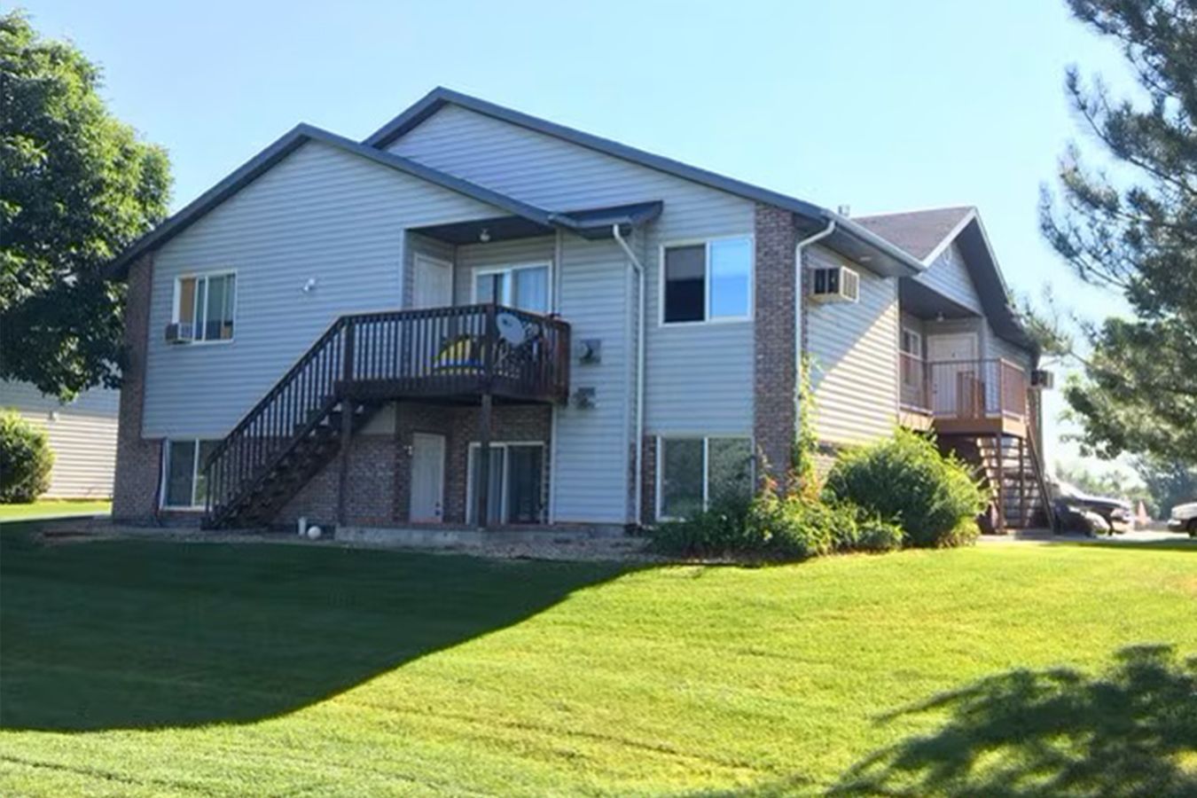 Two-story apartment building with green lawn and wooden deck. Blue sky.