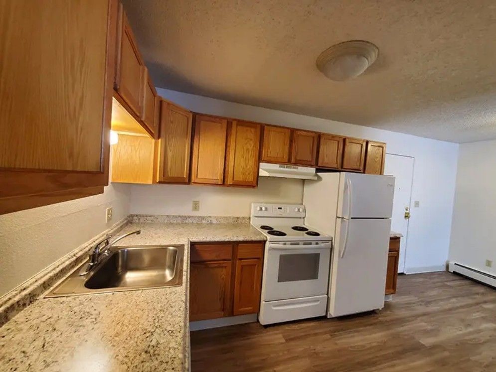 Kitchen with wooden cabinets, white appliances, and speckled countertops.