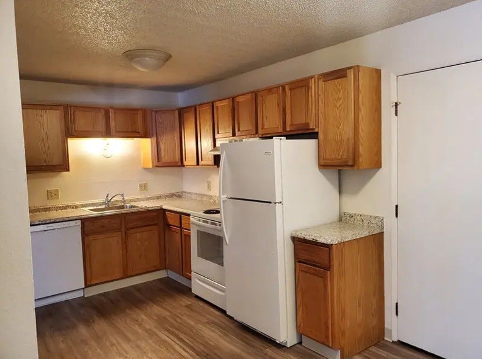 Kitchen with wood cabinets, white appliances, and laminate flooring.