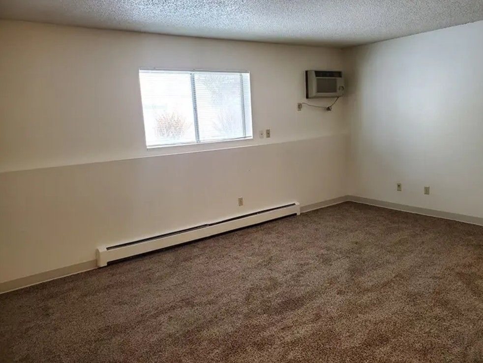 Empty room with beige walls, brown carpet, window, and air conditioner.