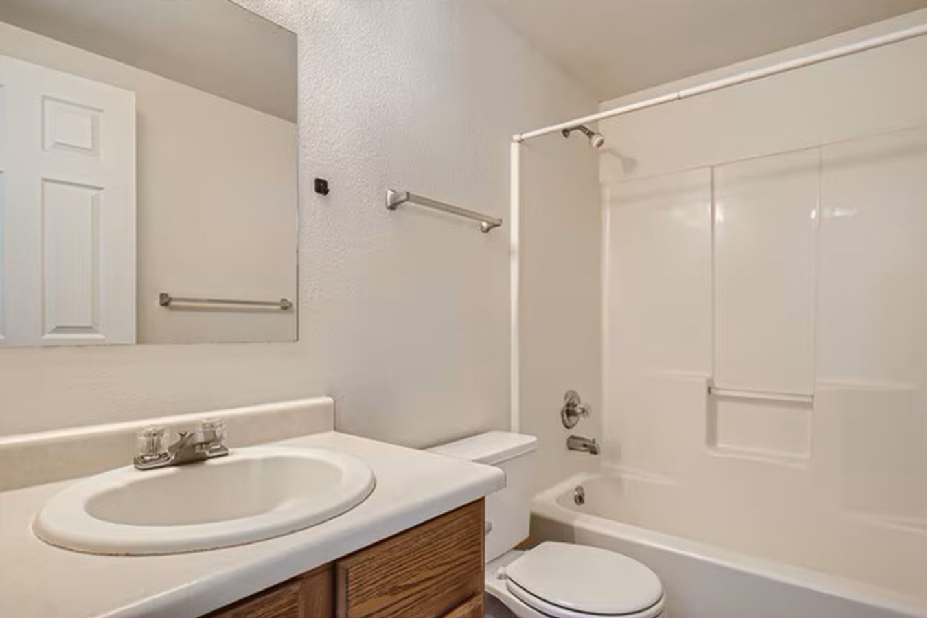 Bathroom with white fixtures, vanity with sink, toilet, bathtub with shower surround.