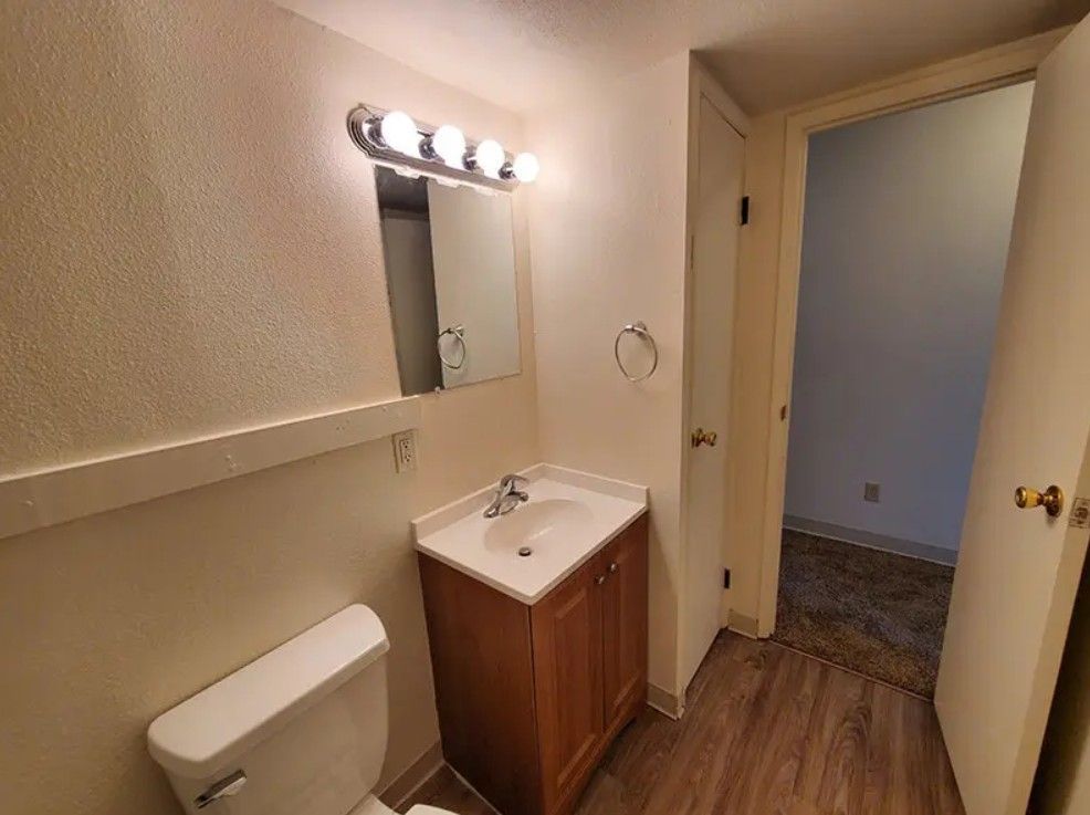 Bathroom with a vanity, toilet, and open doorway to a room.