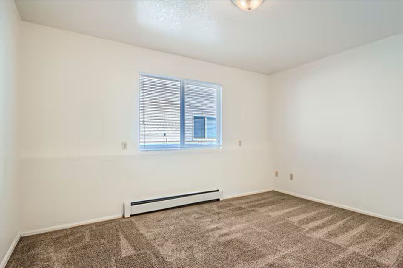 Empty room with brown carpet, white walls, and a window with blinds.