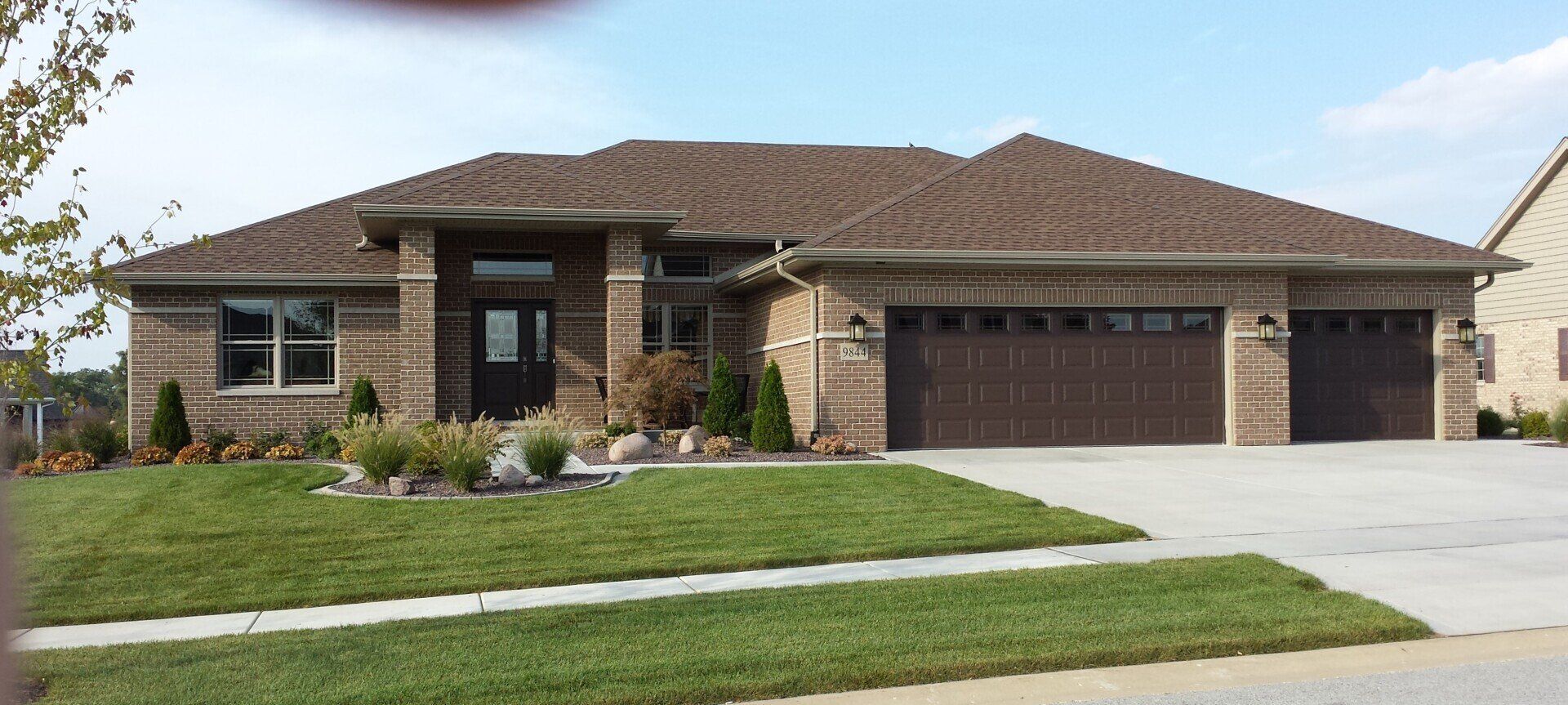 A large brick house with a brown garage door is sitting on top of a lush green lawn.