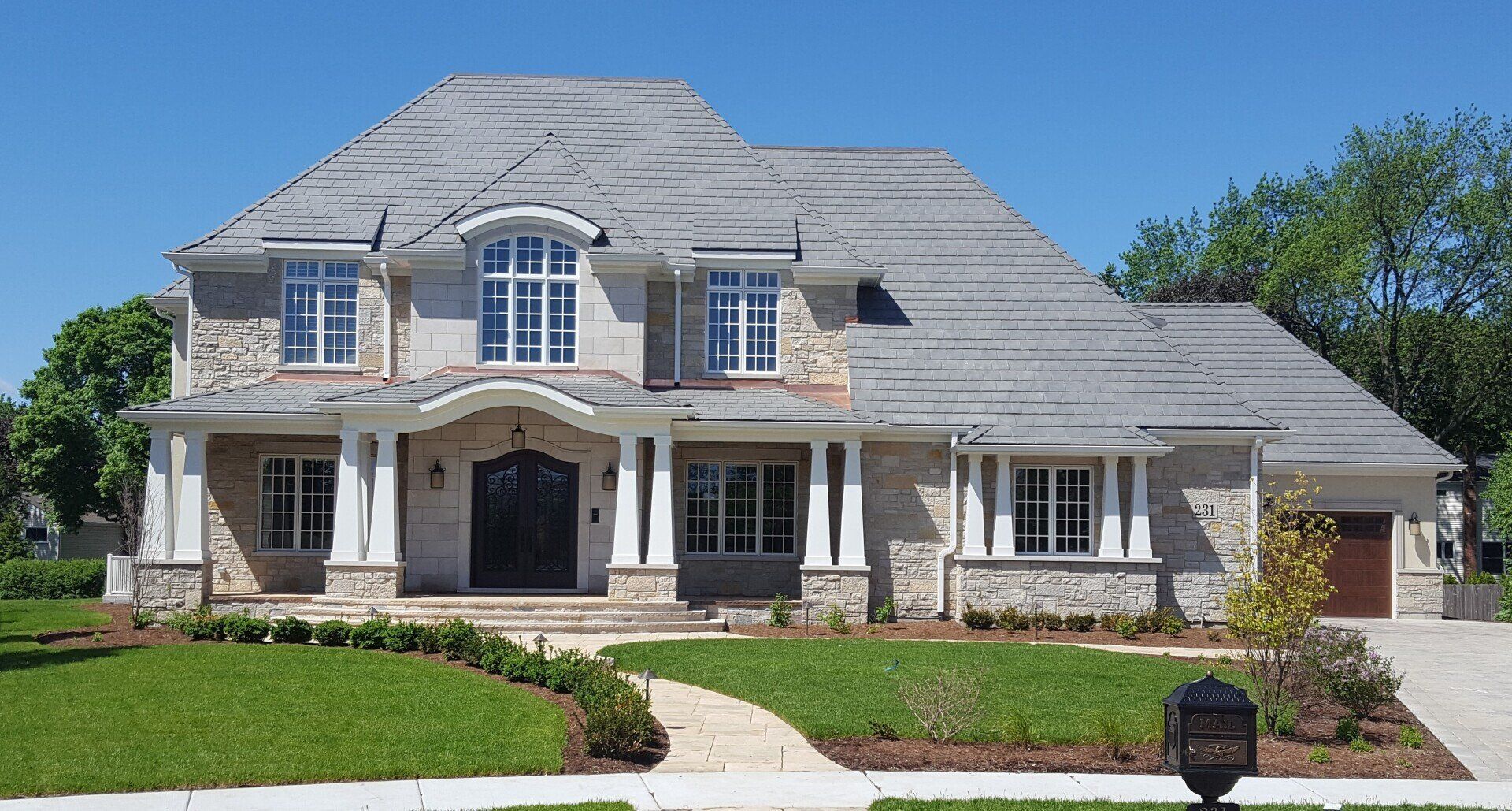 A large house with a gray roof has a mailbox in front of it