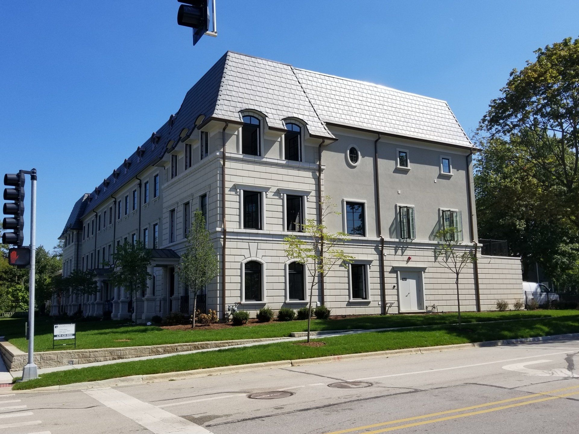 A large building with a gray roof is sitting on the corner of a street.