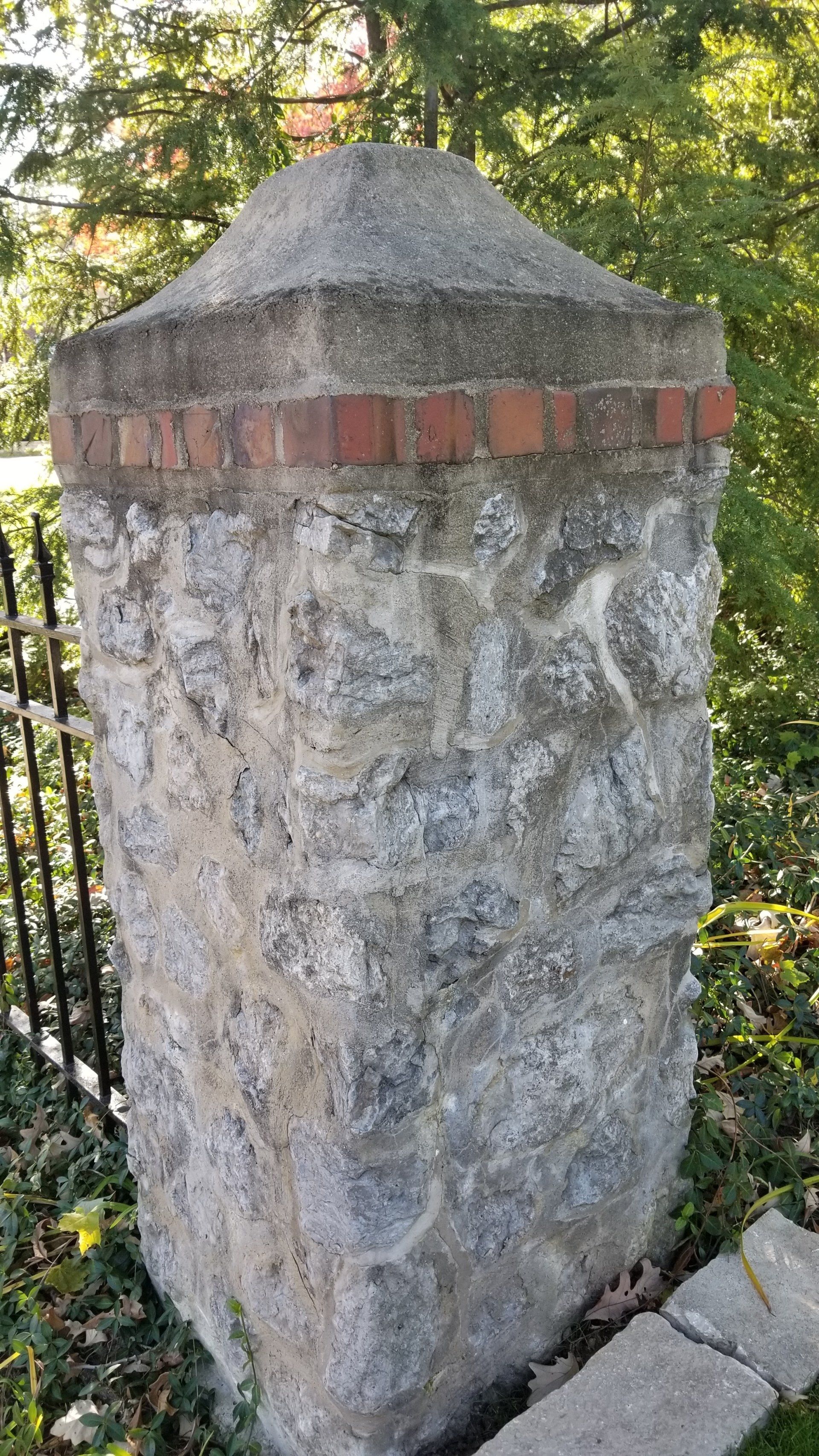 A stone post with a brick border is sitting next to a fence.