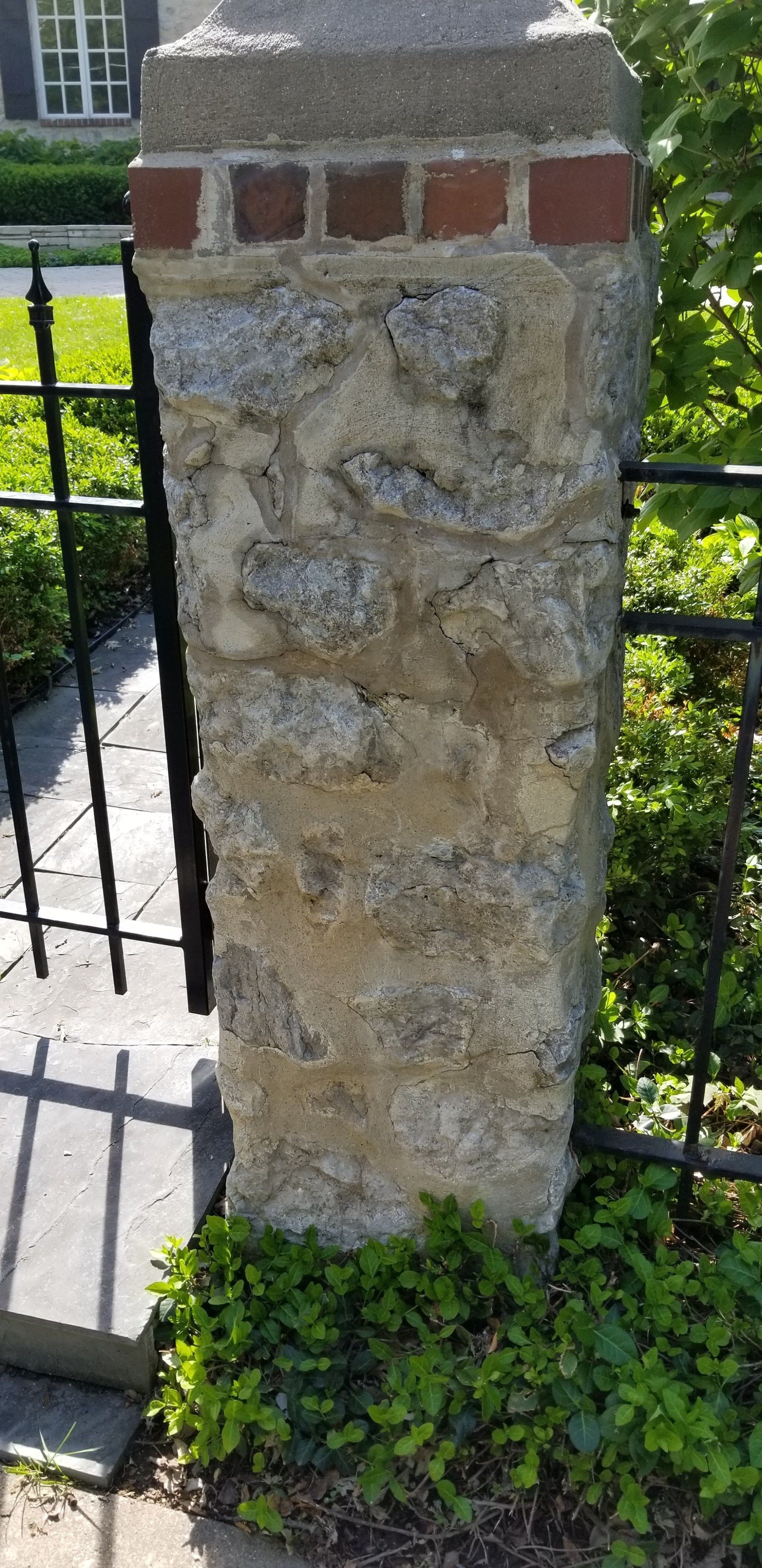 A stone post with bricks on it is next to a gate.