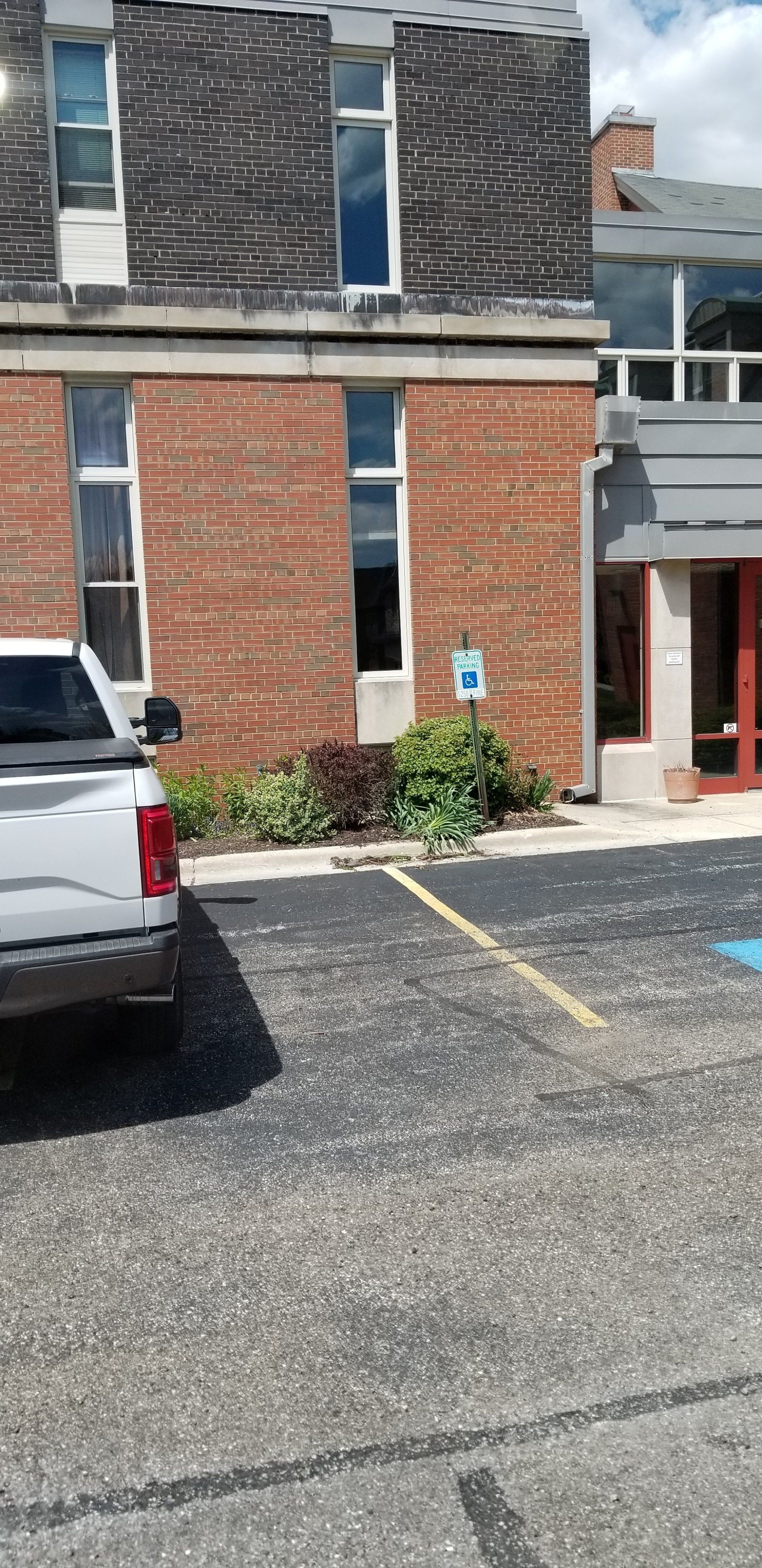 A white truck is parked in a handicapped parking spot in front of a brick building.