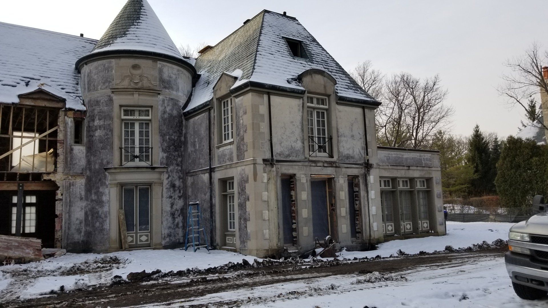 An old abandoned house in the snow with a car parked in front of it
