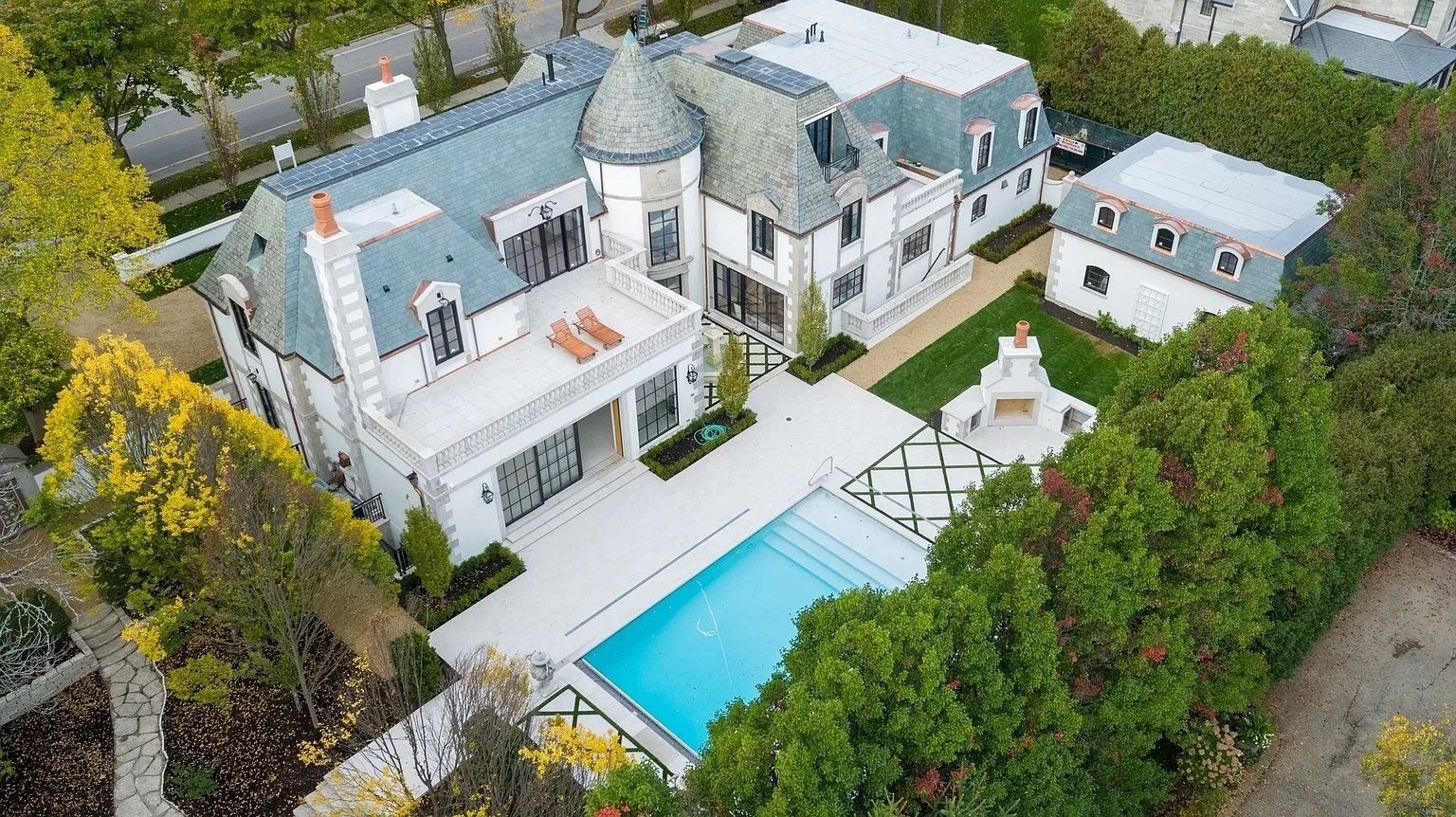 An aerial view of a large white house with a swimming pool surrounded by trees.