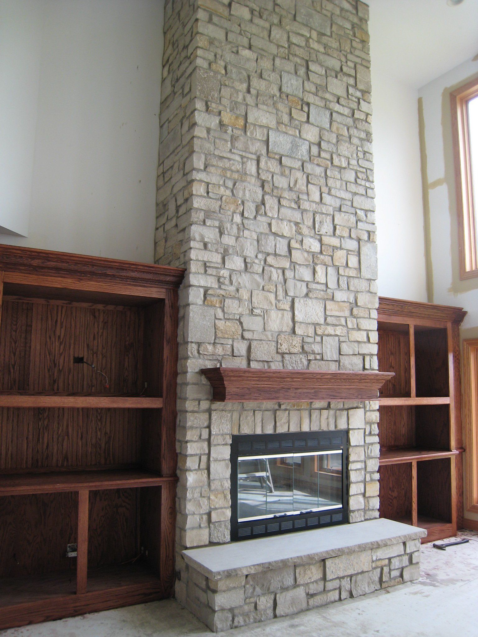 A living room with a stone fireplace and wooden shelves