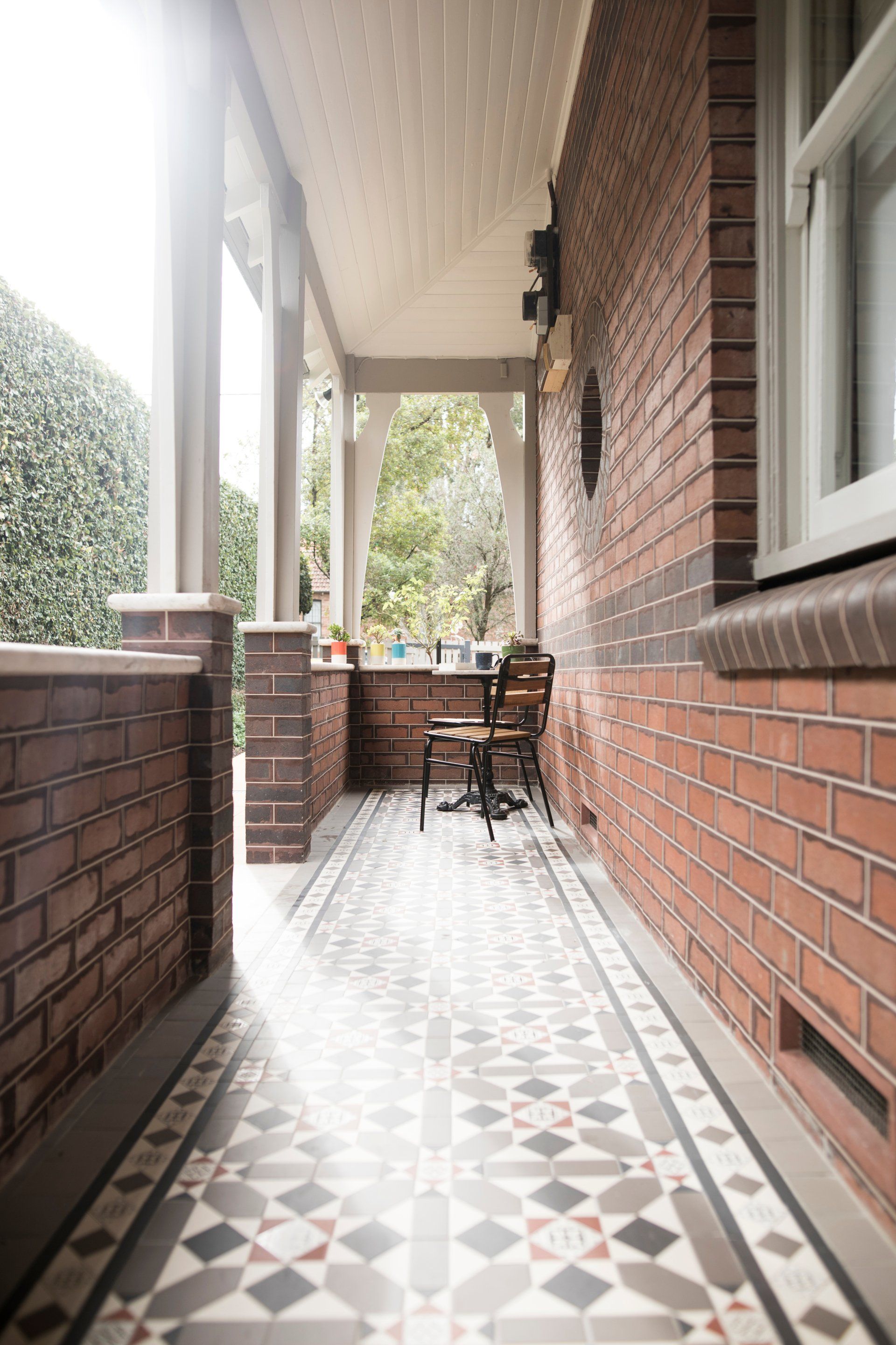 A brick porch with a tiled floor and a table and chairs on it.