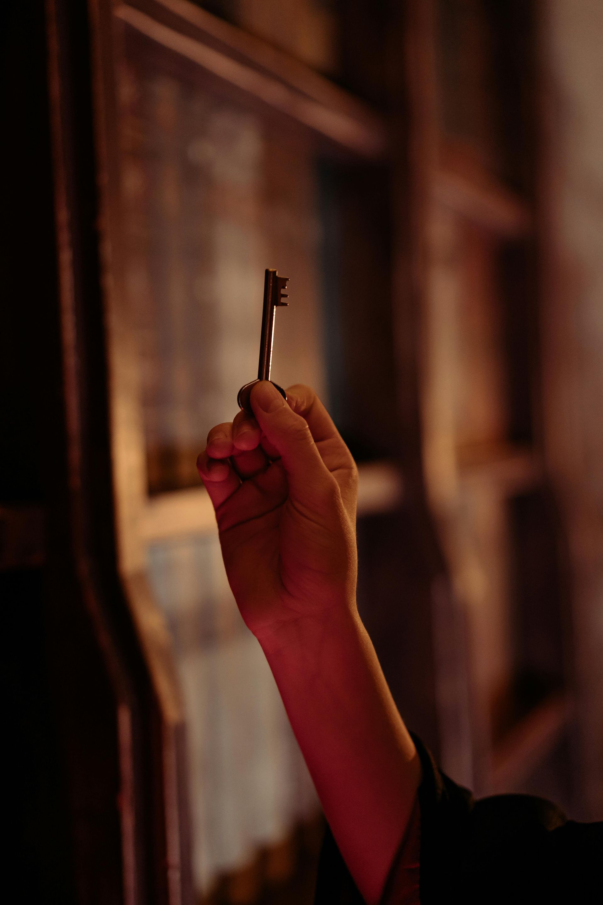 Hand holding a key, against a dark wooden background.