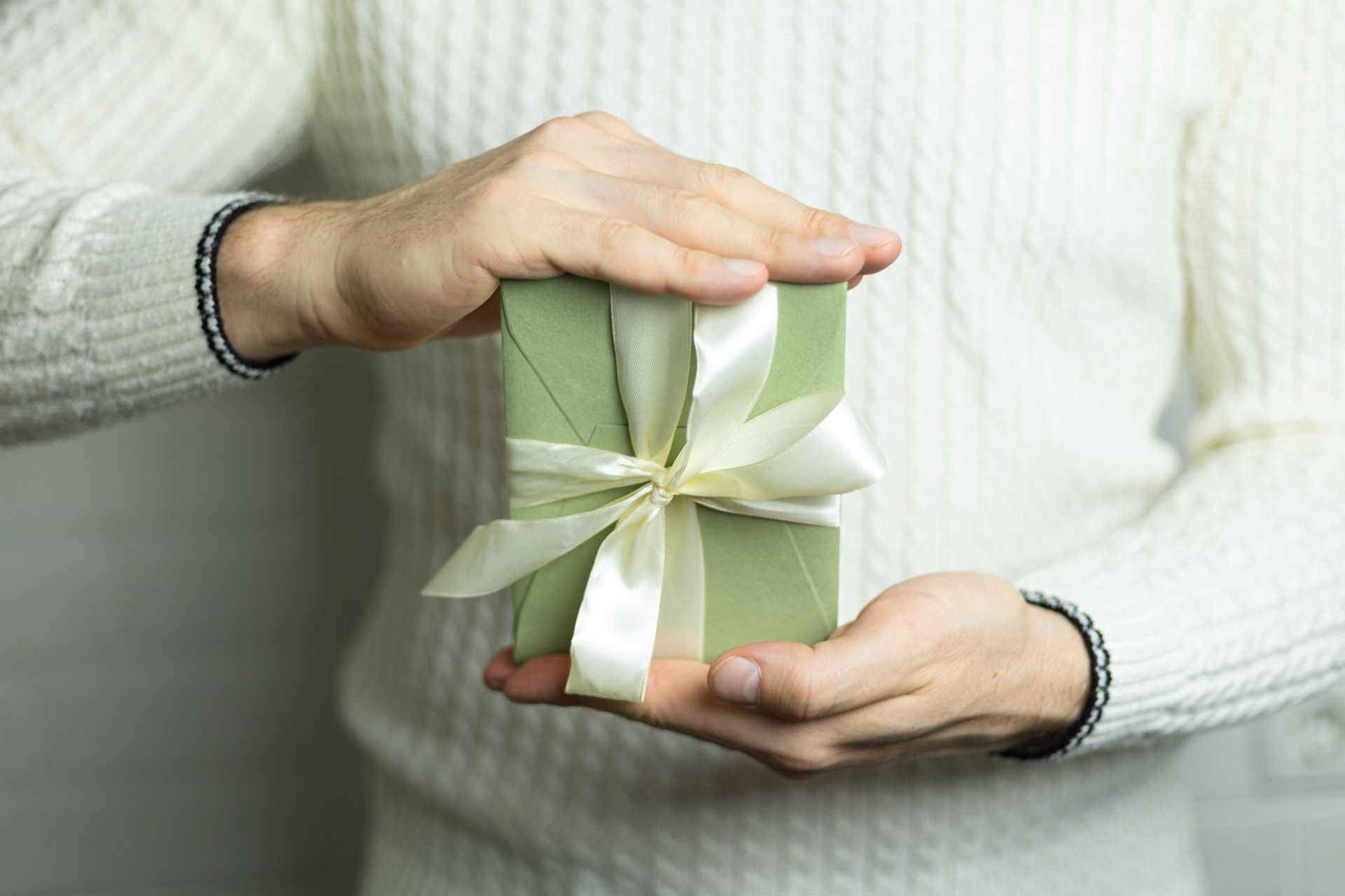 A man in a white sweater is holding a green gift box with a white ribbon.